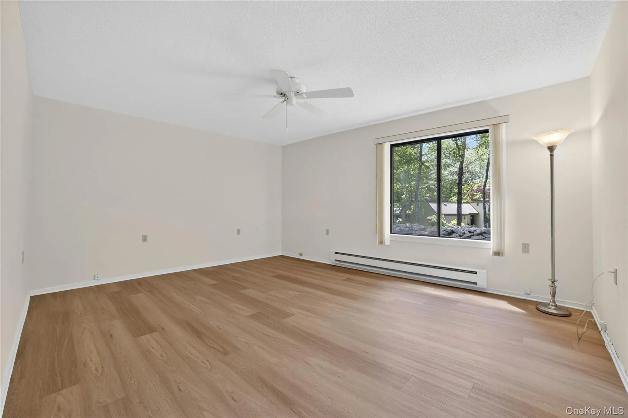 Spacious room featuring wood-finish flooring, a large window, and a ceiling fan Spacious room featuring wood-finish flooring, a large window, and a ceiling fan