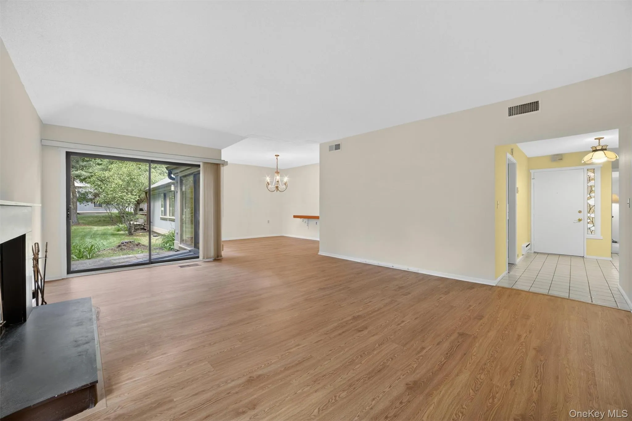 Spacious living area featuring wood-finish flooring, a fireplace with a dark hearth, and a large sliding glass door opening to the backyard Spacious living area featuring wood-finish flooring, a fireplace with a dark hearth, and a large sliding glass door opening to the backyard