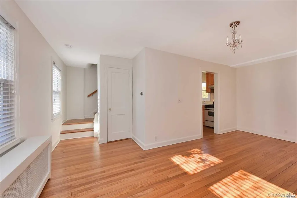 Empty room with radiator, stairway, a chandelier, and light wood-style flooring Empty room with radiator, stairway, a chandelier, and light wood-style flooring