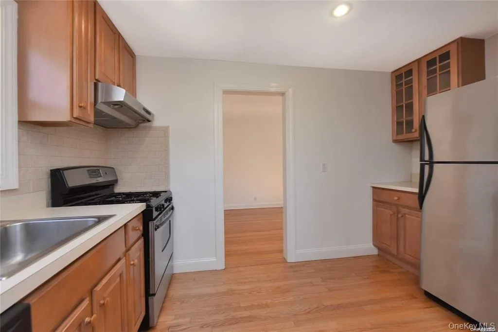 Kitchen featuring stainless steel appliances, under cabinet range hood, light wood finished floors, light countertops, and decorative backsplash Kitchen featuring stainless steel appliances, under cabinet range hood, light wood finished floors, light countertops, and decorative backsplash