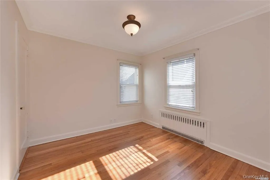 Empty room featuring radiator heating unit, light wood-style flooring, and ornamental molding Empty room featuring radiator heating unit, light wood-style flooring, and ornamental molding