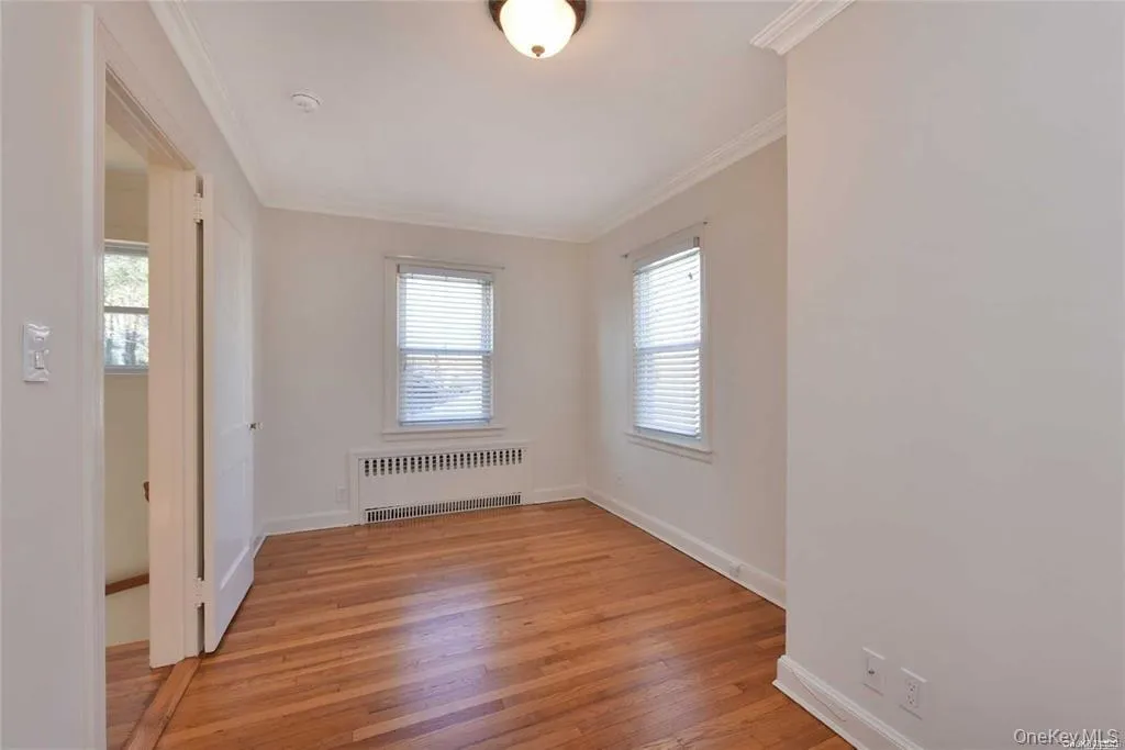 Empty room featuring radiator heating unit, light wood-style flooring, and ornamental molding Empty room featuring radiator heating unit, light wood-style flooring, and ornamental molding