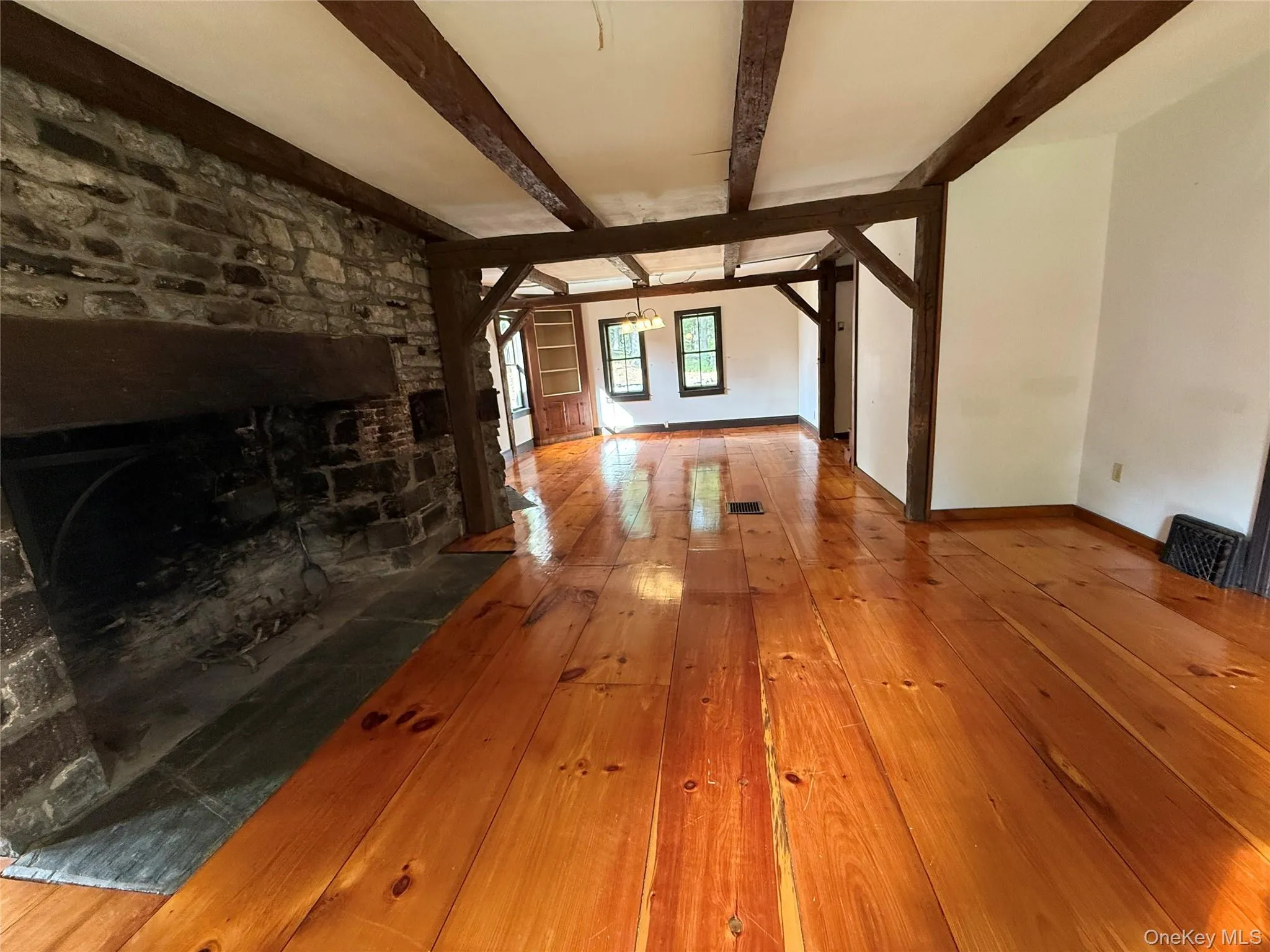 Unfurnished living room with hardwood / wood-style flooring, beamed ceiling, and a chandelier Unfurnished living room with hardwood / wood-style flooring, beamed ceiling, and a chandelier