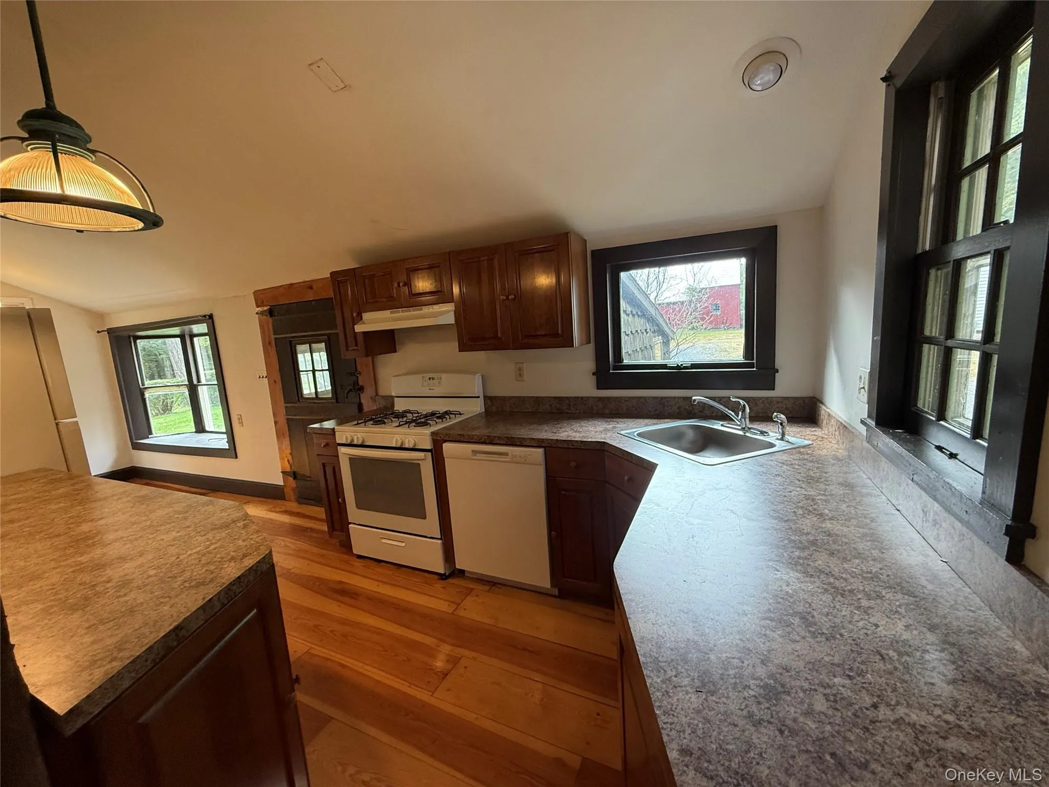 Kitchen featuring white appliances, lofted ceiling, light wood finished floors, decorative light fixtures, and under cabinet range hood Kitchen featuring white appliances, lofted ceiling, light wood finished floors, decorative light fixtures, and under cabinet range hood
