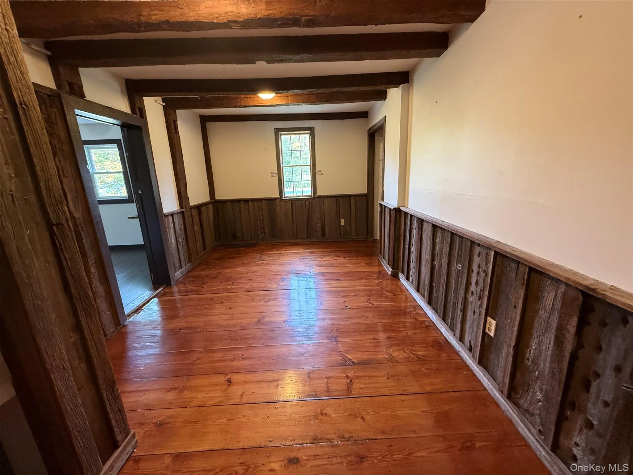 Empty room featuring a wainscoted wall, wood-type flooring, wood walls, and beamed ceiling Empty room featuring a wainscoted wall, wood-type flooring, wood walls, and beamed ceiling