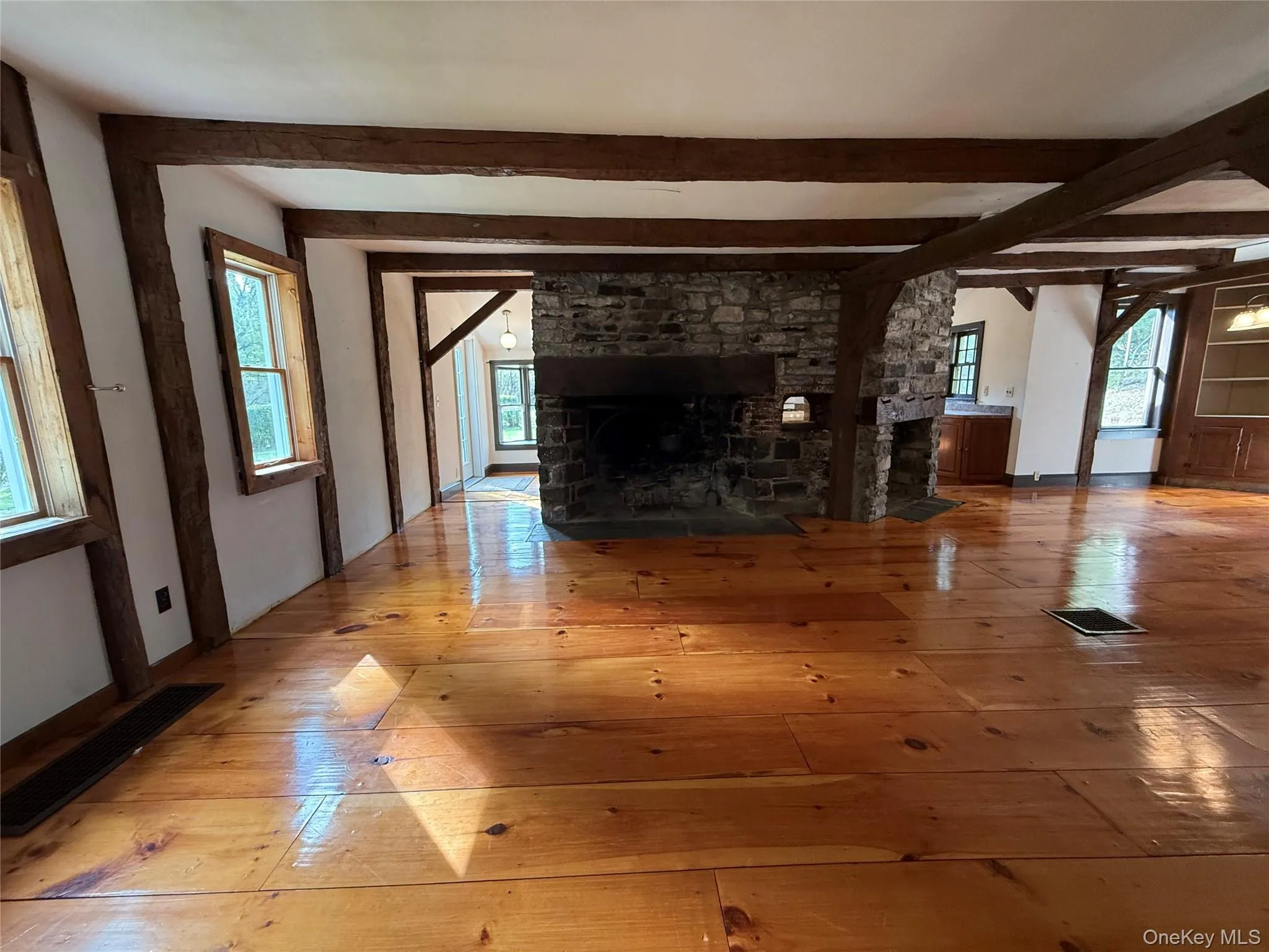 Unfurnished living room with hardwood / wood-style floors, a stone fireplace, healthy amount of natural light, and beamed ceiling Unfurnished living room with hardwood / wood-style floors, a stone fireplace, healthy amount of natural light, and beamed ceiling
