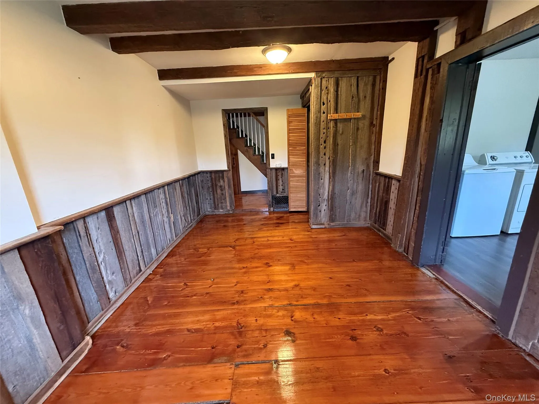 Hall with wood-type flooring, a wainscoted wall, beamed ceiling, wooden walls, and stairway Hall with wood-type flooring, a wainscoted wall, beamed ceiling, wooden walls, and stairway