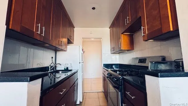 Kitchen featuring light tile patterned flooring, range with gas stovetop, backsplash, freestanding refrigerator, and dark stone counters Kitchen featuring light tile patterned flooring, range with gas stovetop, backsplash, freestanding refrigerator, and dark stone counters