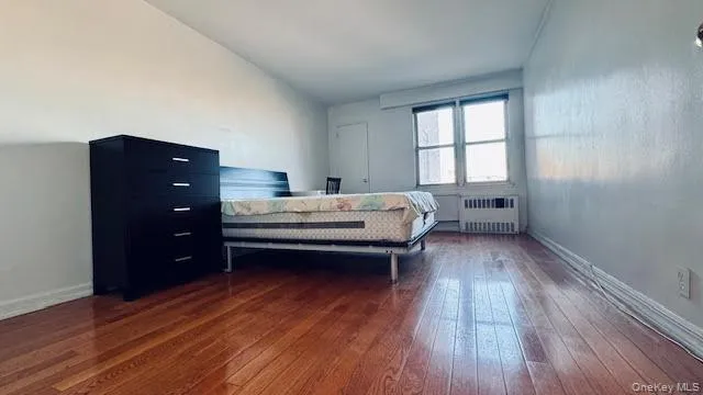 Bedroom featuring radiator heating unit and dark wood-style floors Bedroom featuring radiator heating unit and dark wood-style floors