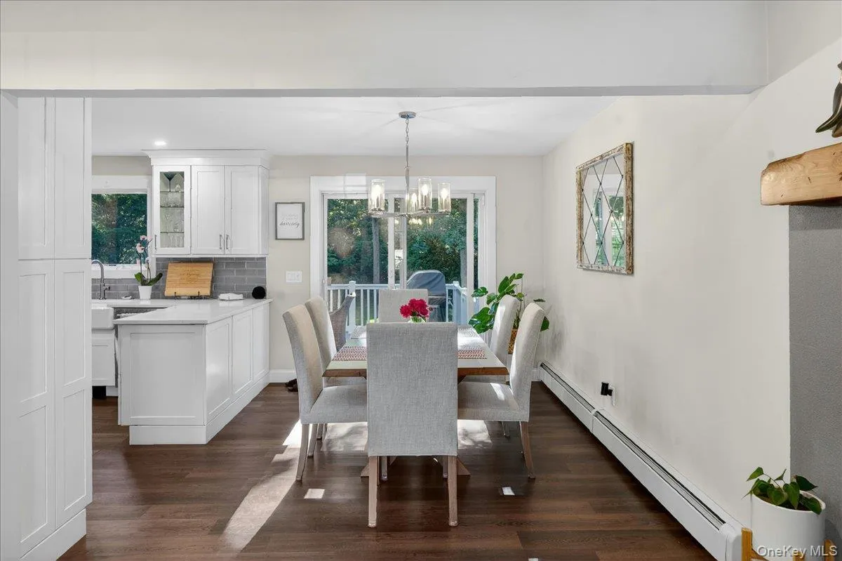 Open-concept dining area featuring wood-finish flooring, a contemporary chandelier, and a white railing deck access Open-concept dining area featuring wood-finish flooring, a contemporary chandelier, and a white railing deck access