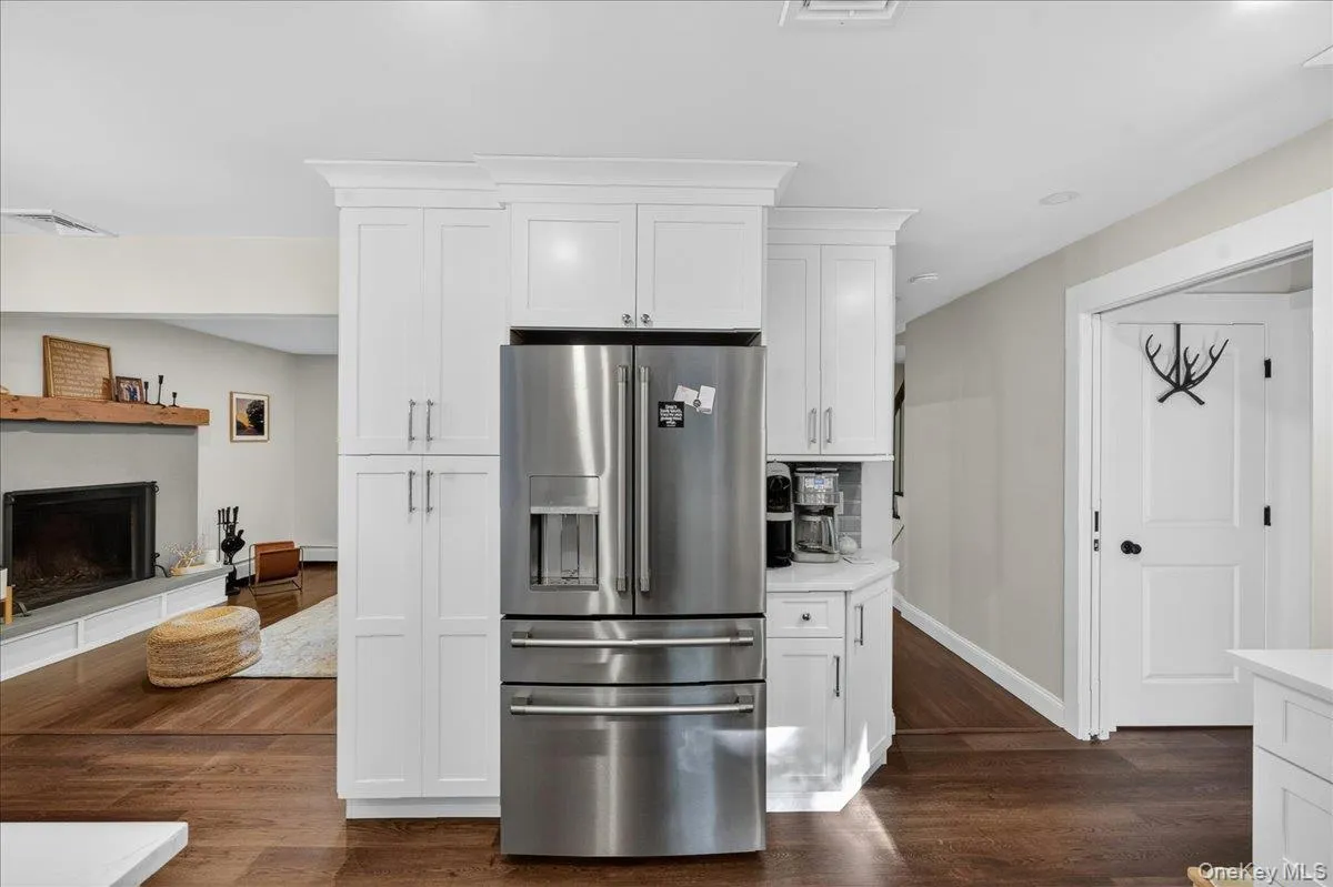 Kitchen featuring white shaker-style cabinetry, a stainless steel refrigerator, and wood-finish flooring Kitchen featuring white shaker-style cabinetry, a stainless steel refrigerator, and wood-finish flooring