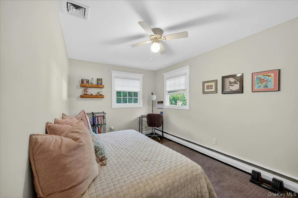 Light-filled room featuring two windows with white blinds, a ceiling fan with integrated lighting, wood-finish flooring, and light-toned walls Light-filled room featuring two windows with white blinds, a ceiling fan with integrated lighting, wood-finish flooring, and light-toned walls