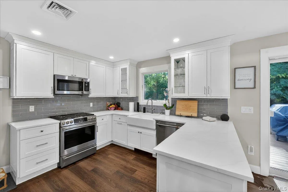 Modern kitchen featuring white shaker cabinetry, stainless steel appliances, white countertops, a gray subway tile backsplash, and wood-finish flooring Modern kitchen featuring white shaker cabinetry, stainless steel appliances, white countertops, a gray subway tile backsplash, and wood-finish flooring