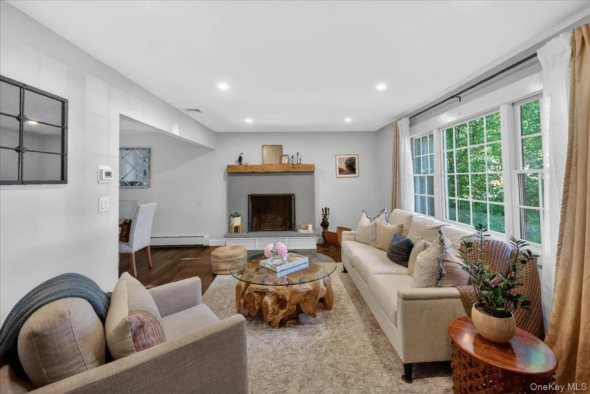 Spacious living area featuring a stone-clad fireplace with a wood mantel, recessed lighting, large windows, and dark wood-finish flooring Spacious living area featuring a stone-clad fireplace with a wood mantel, recessed lighting, large windows, and dark wood-finish flooring