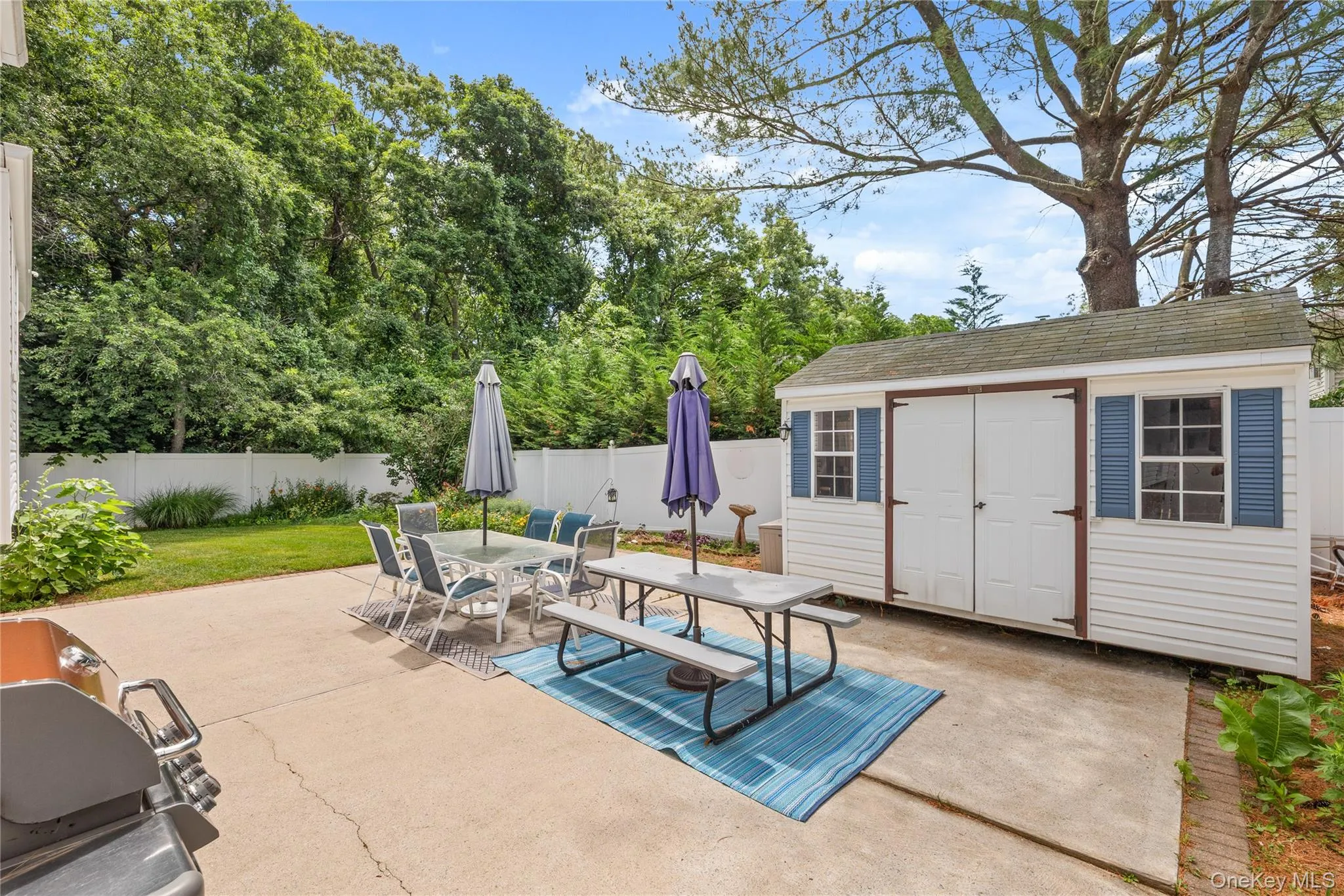 Expansive backyard featuring a concrete patio, grassy areas, and a white privacy fence Expansive backyard featuring a concrete patio, grassy areas, and a white privacy fence