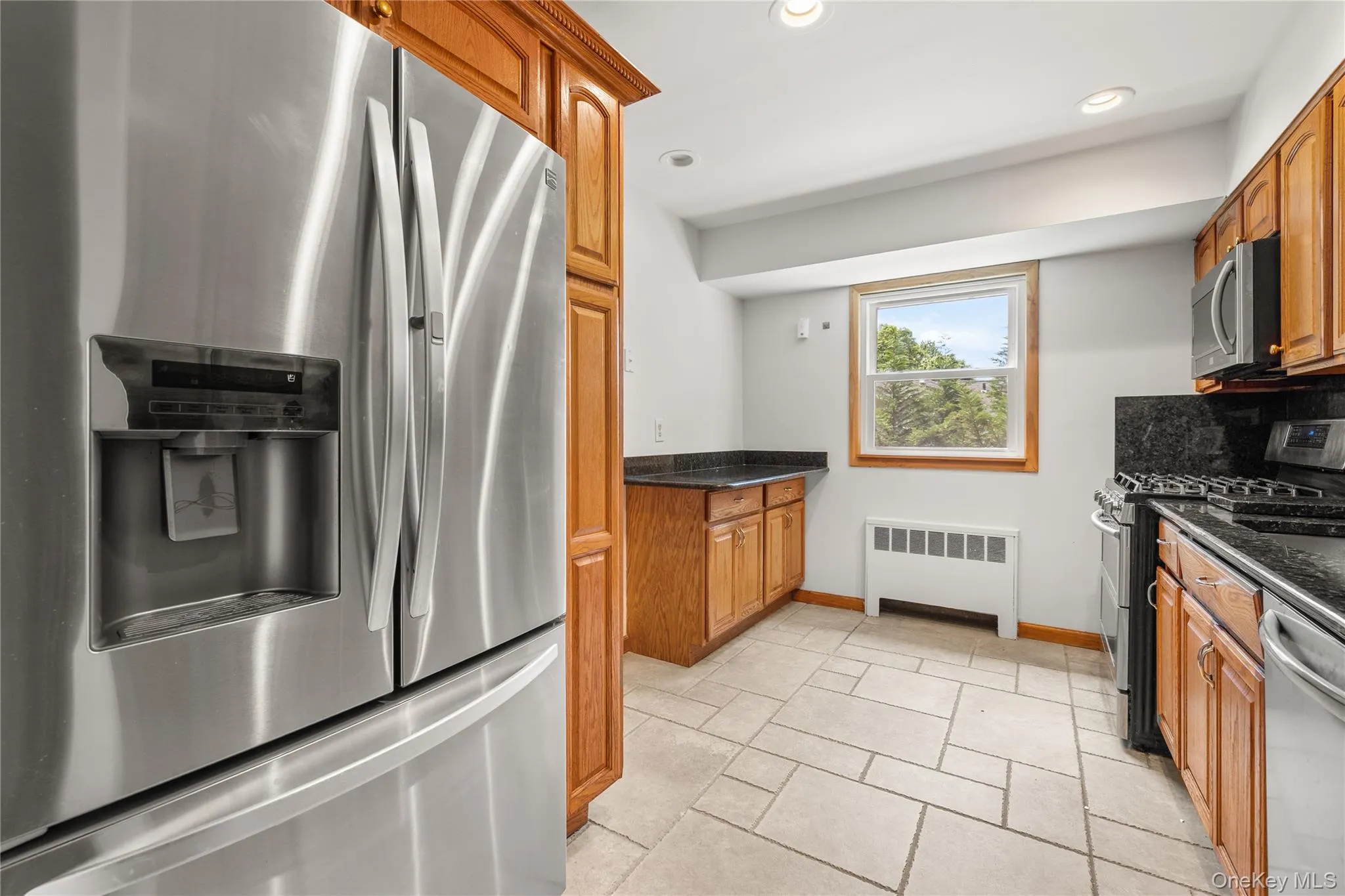Kitchen featuring stainless steel appliances, wood cabinetry, dark countertops, and tile flooring Kitchen featuring stainless steel appliances, wood cabinetry, dark countertops, and tile flooring