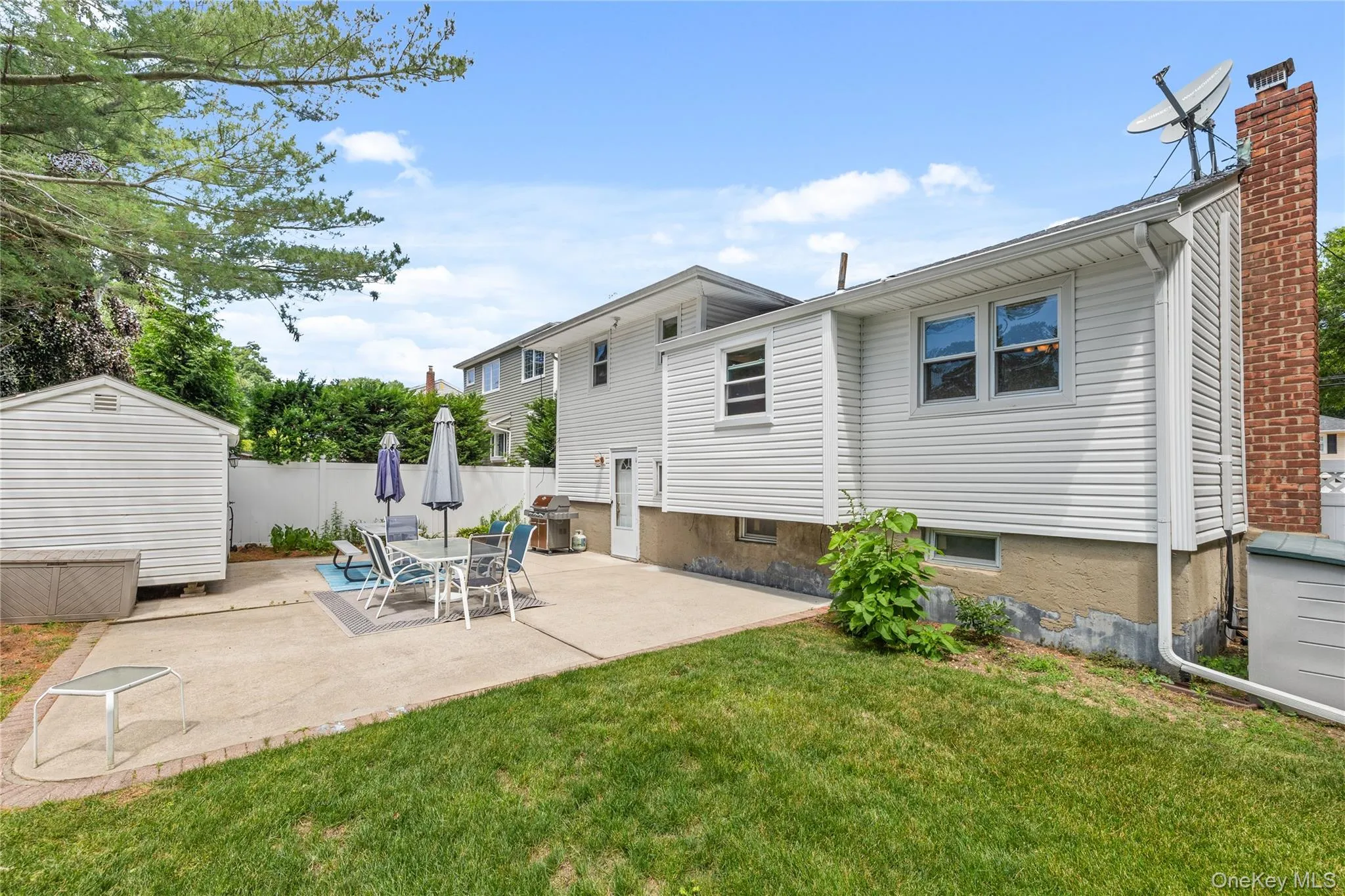 Expansive backyard featuring a concrete patio, grassy areas, and a white privacy fence Expansive backyard featuring a concrete patio, grassy areas, and a white privacy fence