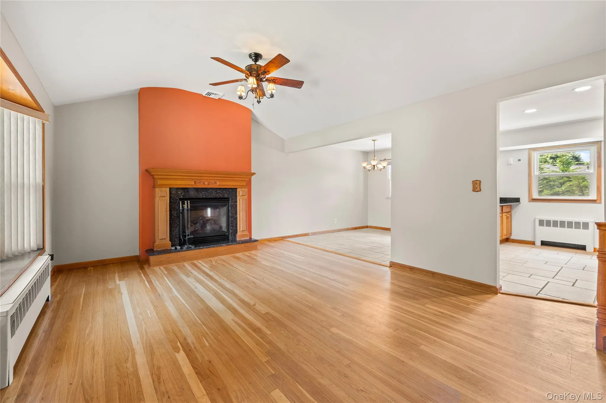 Living space featuring wood-finish flooring, a fireplace with a black stone surround and wood mantel, vaulted ceilings, and a ceiling fan Living space featuring wood-finish flooring, a fireplace with a black stone surround and wood mantel, vaulted ceilings, and a ceiling fan