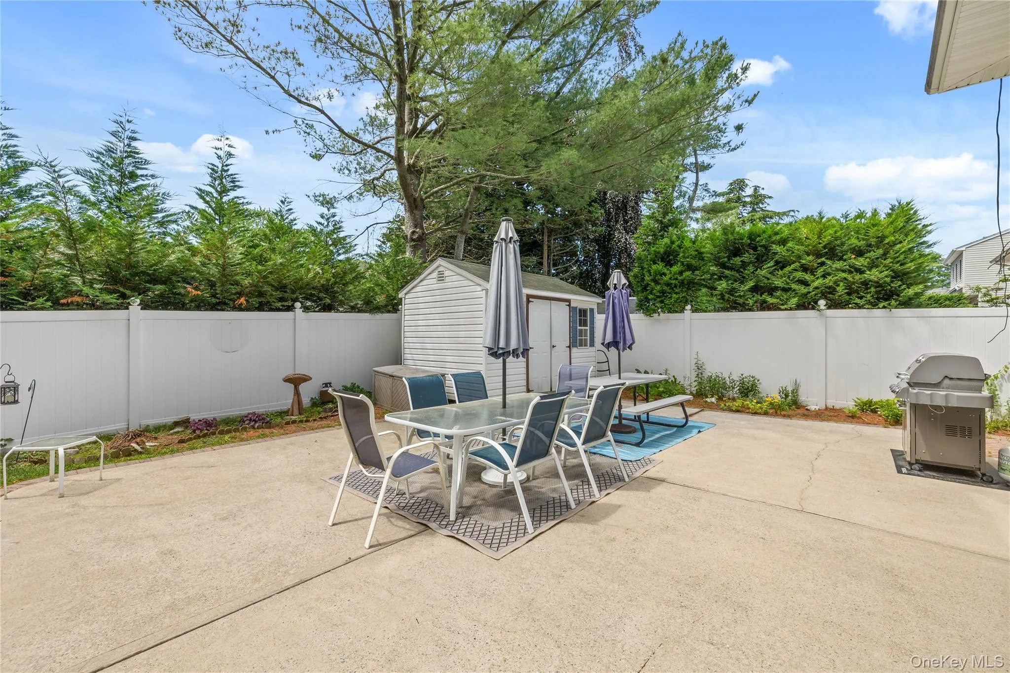 Expansive backyard featuring a concrete patio, grassy areas, and a white privacy fence Expansive backyard featuring a concrete patio, grassy areas, and a white privacy fence