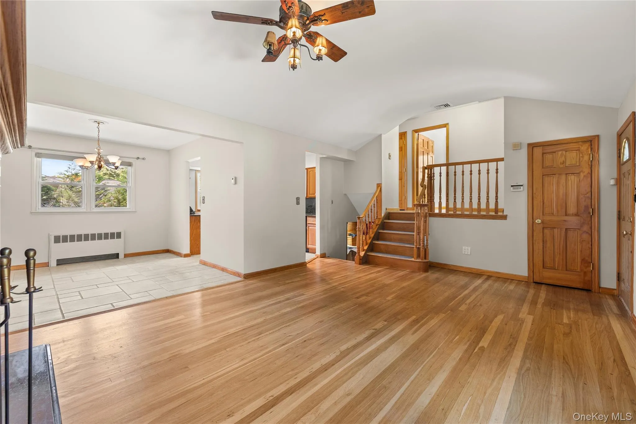 Spacious living and dining room featuring polished wood-finish flooring, a ceiling fan with integrated lighting, and a prominent staircase with wood railing Spacious living and dining room featuring polished wood-finish flooring, a ceiling fan with integrated lighting, and a prominent staircase with wood railing