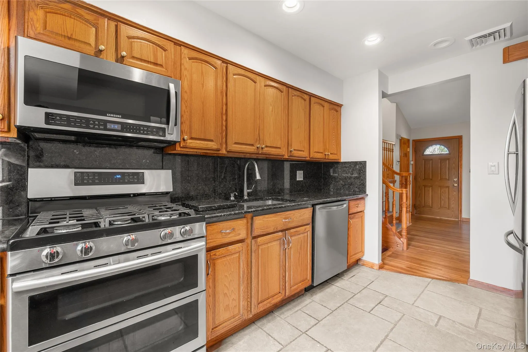 Kitchen featuring wood cabinetry, black countertops, stainless steel appliances, and tile flooring Kitchen featuring wood cabinetry, black countertops, stainless steel appliances, and tile flooring