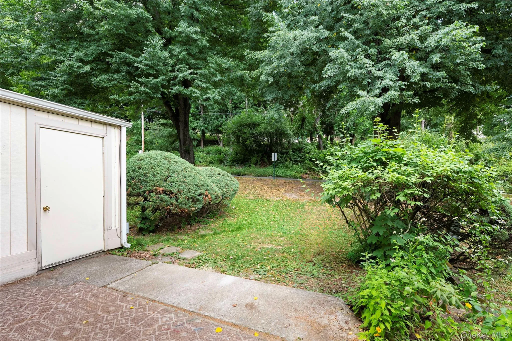 Utility shed with a side-hinged door, concrete pad, patterned hardscaping, lush green lawn, and mature trees Utility shed with a side-hinged door, concrete pad, patterned hardscaping, lush green lawn, and mature trees