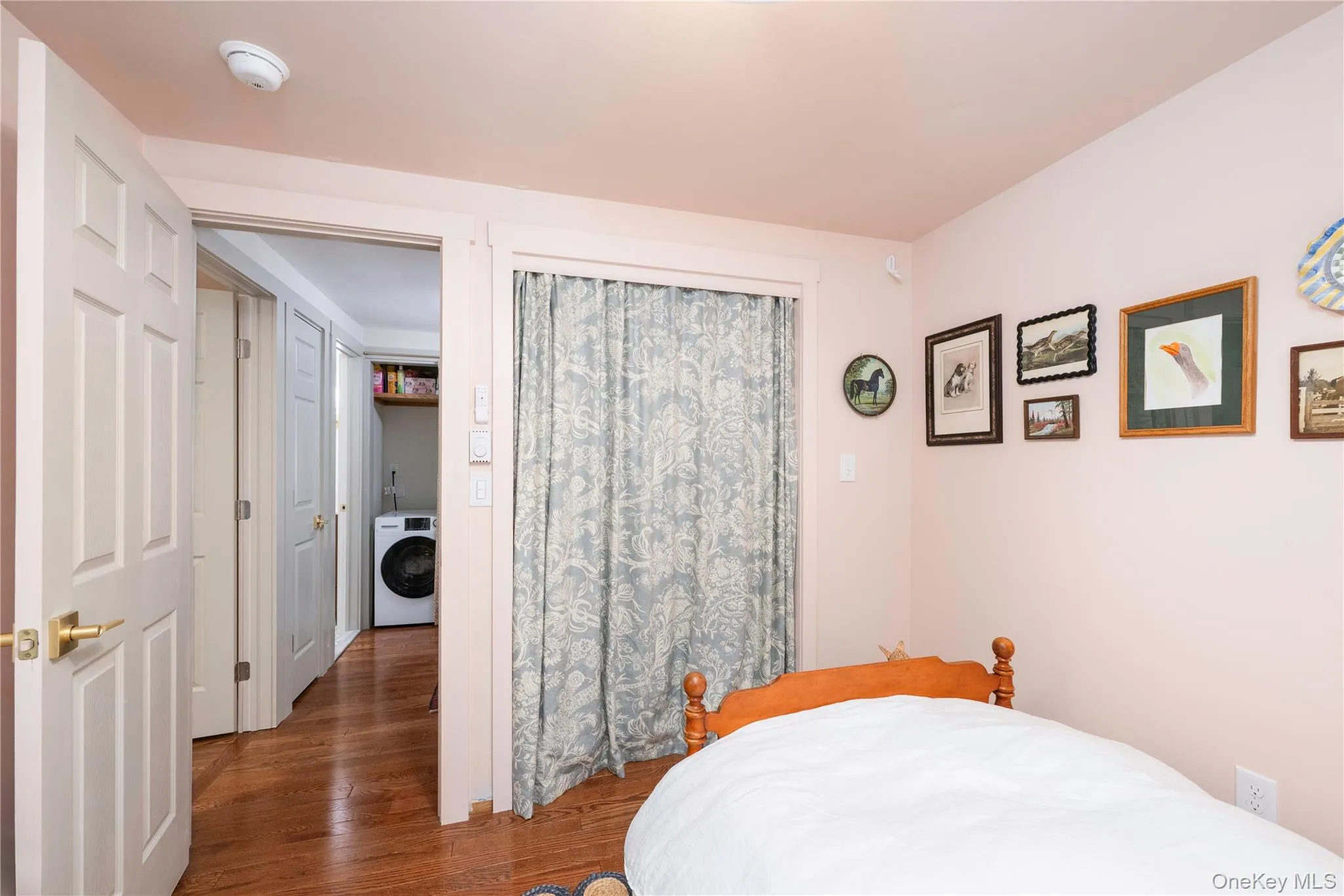 Bedroom with wood flooring, featuring a built-in closet with privacy curtains, and a solid core door with brass hardware Bedroom with wood flooring, featuring a built-in closet with privacy curtains, and a solid core door with brass hardware