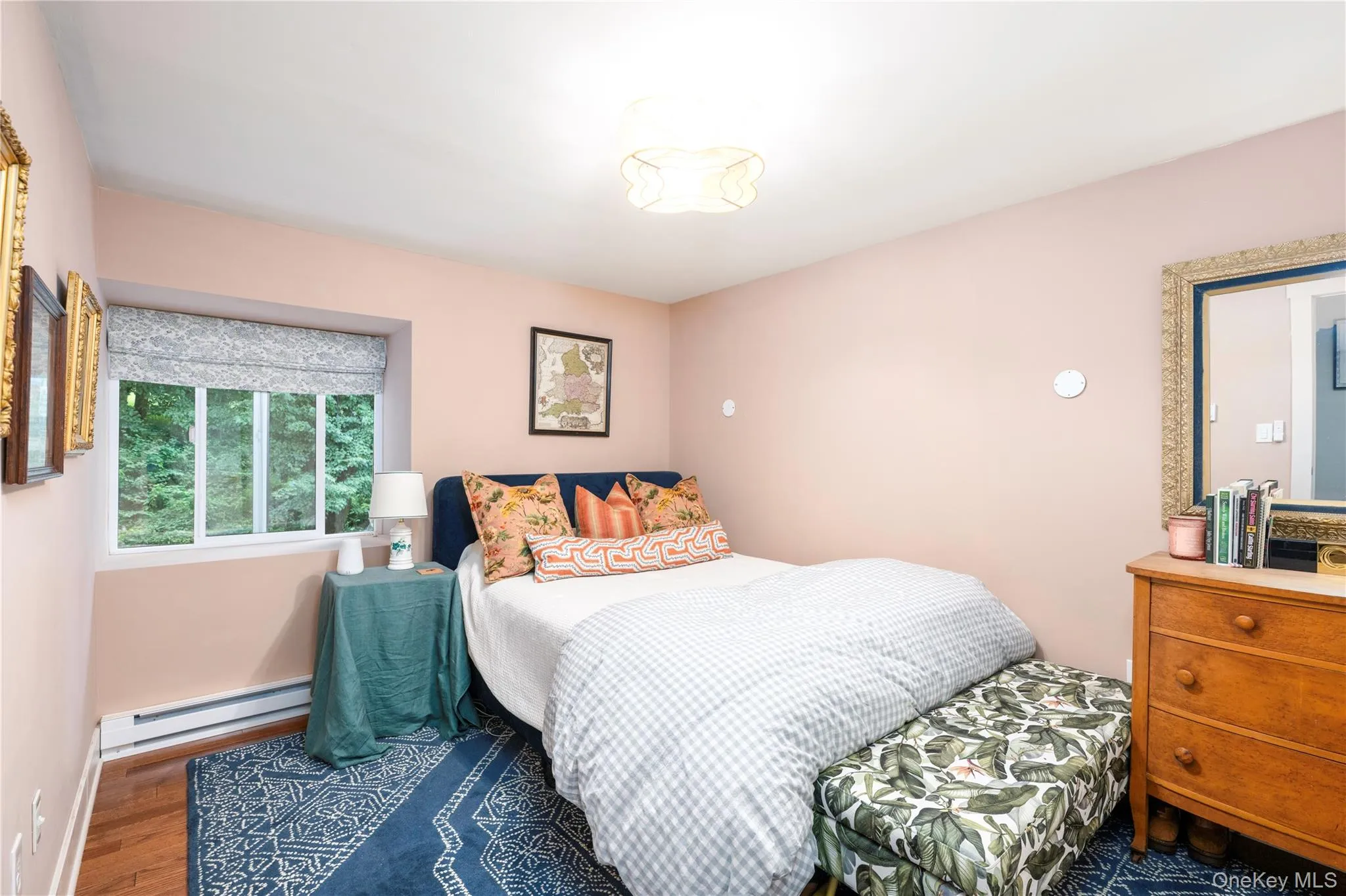 Hardwood flooring throughout this bedroom featuring a window with an exterior landscape, baseboard heating, and a 'Fandelier' ceiling light fixture Hardwood flooring throughout this bedroom featuring a window with an exterior landscape, baseboard heating, and a 'Fandelier' ceiling light fixture