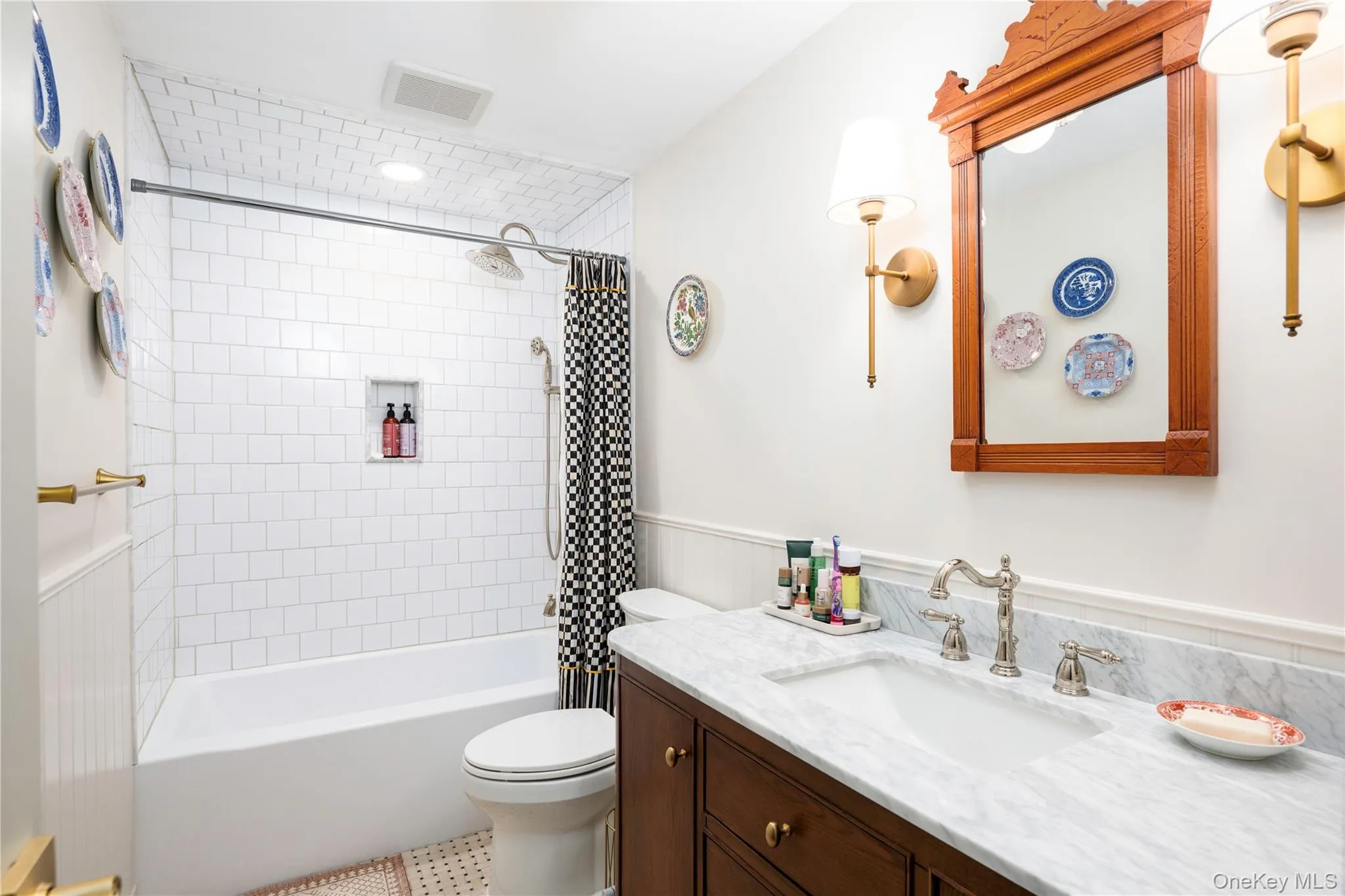 Bathroom featuring a white subway tile shower surround with a built-in niche, a full-size bathtub, a vanity with a white stone countertop, an integrated sink, and an ornate wood-framed mirror Bathroom featuring a white subway tile shower surround with a built-in niche, a full-size bathtub, a vanity with a white stone countertop, an integrated sink, and an ornate wood-framed mirror