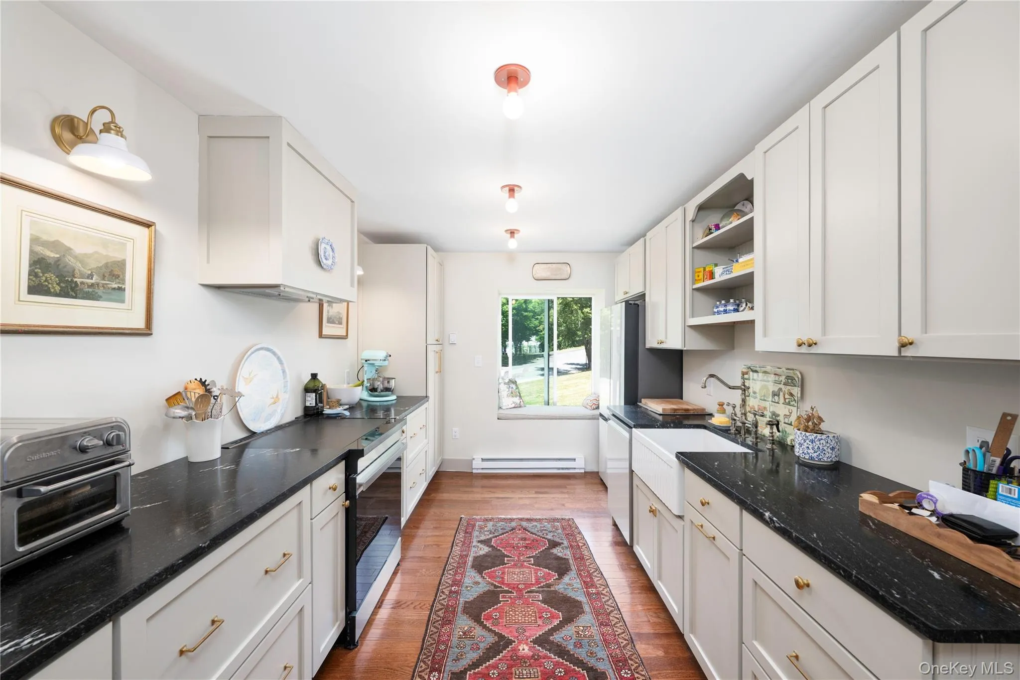 Galley kitchen featuring light-toned cabinetry, dark countertops, a farmhouse sink, integrated appliances, and wood flooring Galley kitchen featuring light-toned cabinetry, dark countertops, a farmhouse sink, integrated appliances, and wood flooring