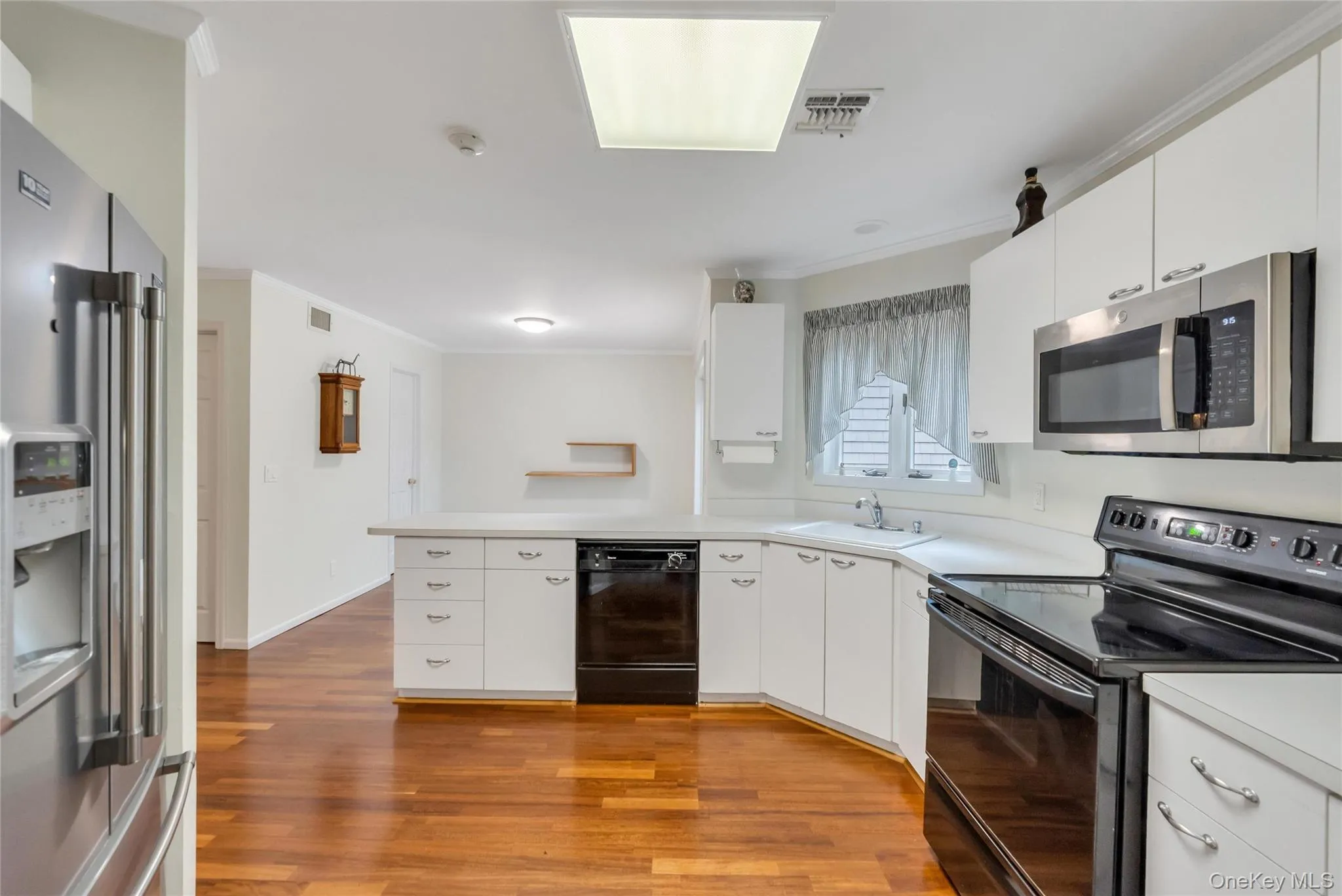 Kitchen featuring wood-finish flooring, white cabinetry, and a suite of stainless steel and black appliances, including a built-in microwave, range, and refrigerator Kitchen featuring wood-finish flooring, white cabinetry, and a suite of stainless steel and black appliances, including a built-in microwave, range, and refrigerator