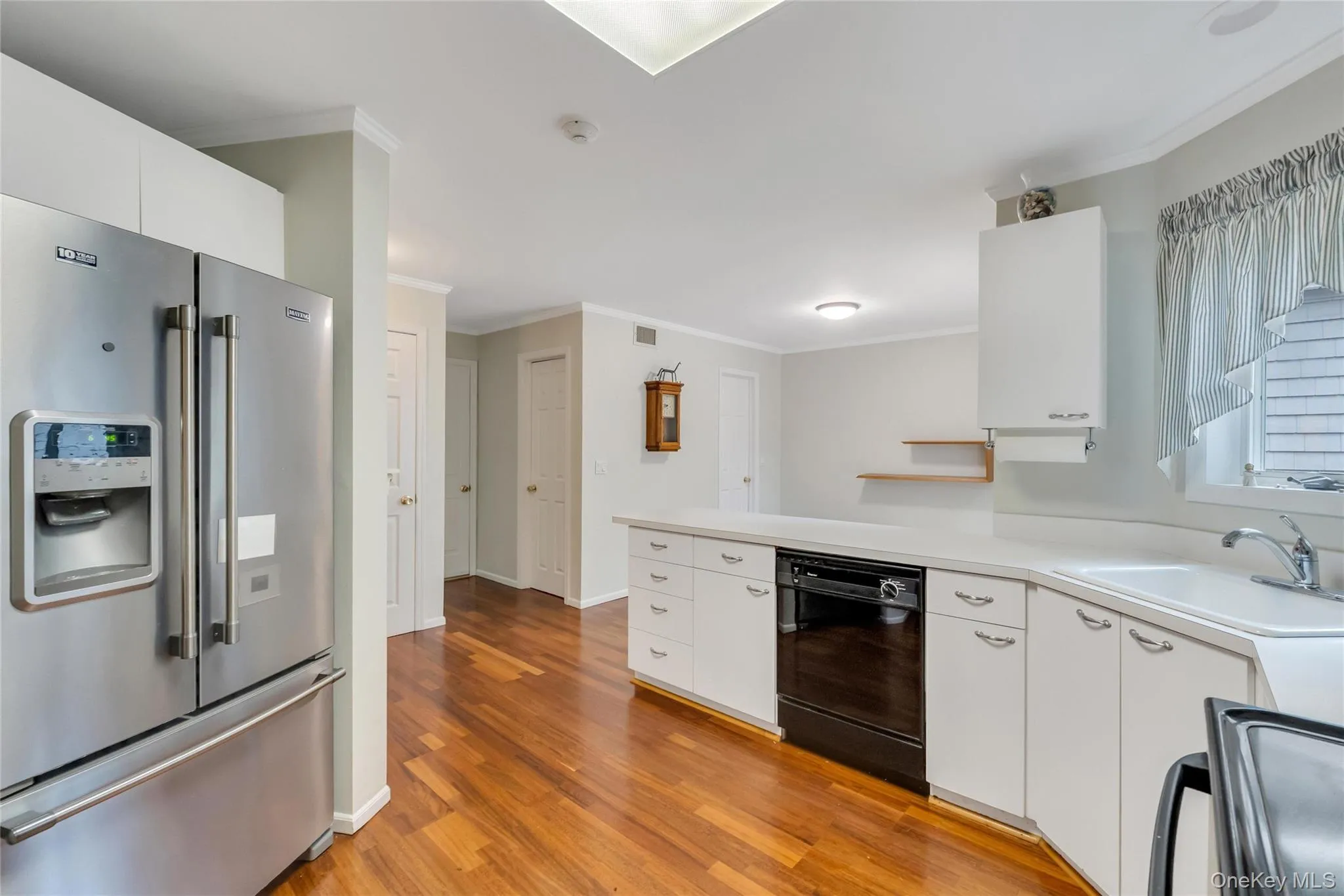 Kitchen featuring wood-finish flooring, white cabinetry, integrated stainless steel refrigerator, and built-in dishwasher Kitchen featuring wood-finish flooring, white cabinetry, integrated stainless steel refrigerator, and built-in dishwasher