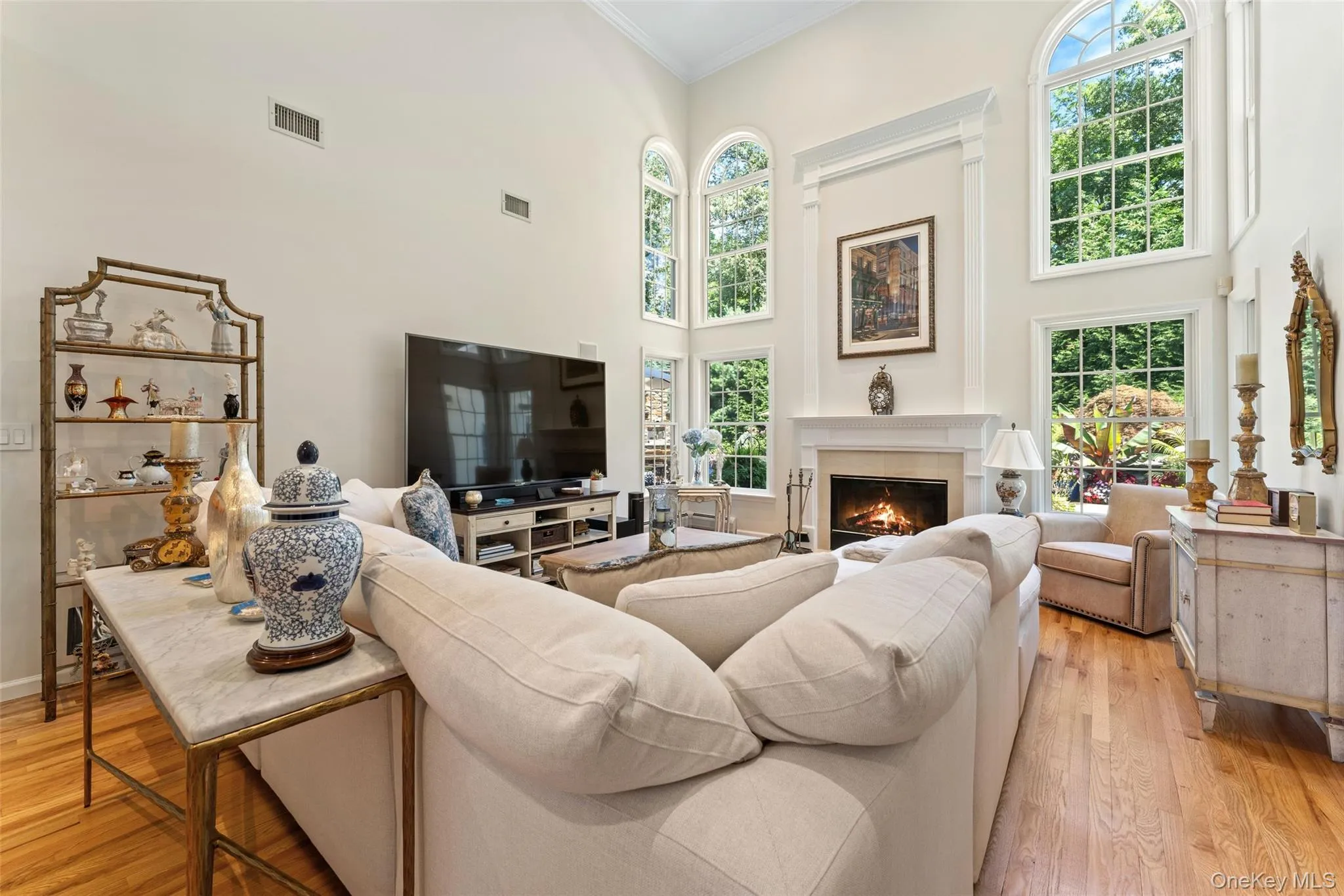 Living area featuring light wood-style floors, crown molding, a warm lit fireplace, and healthy amount of natural light Living area featuring light wood-style floors, crown molding, a warm lit fireplace, and healthy amount of natural light