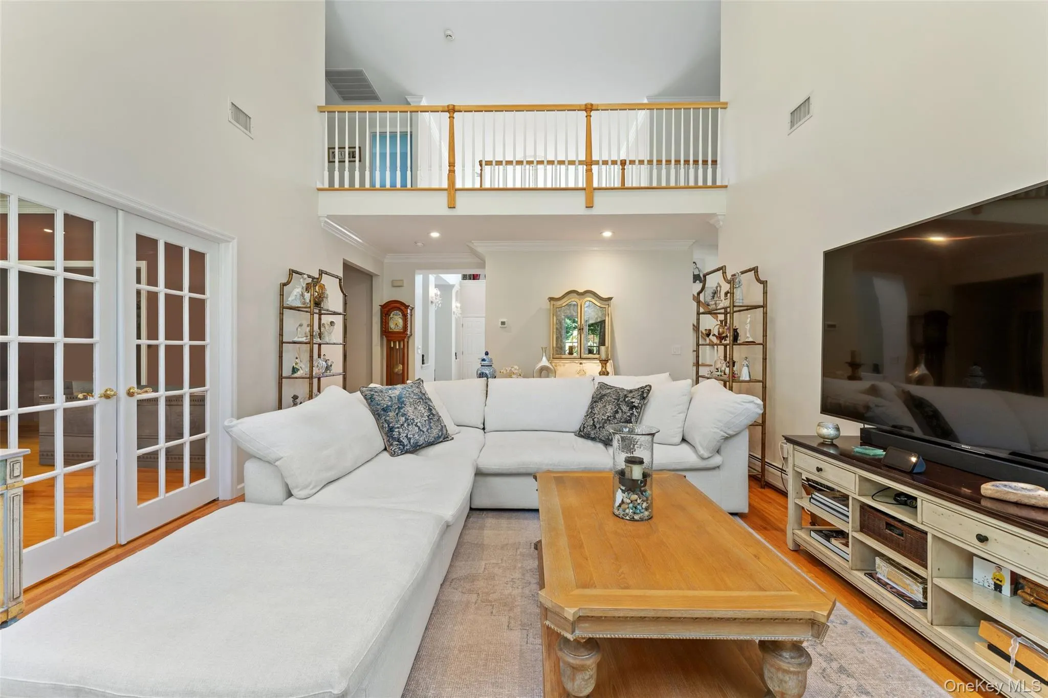 Living room featuring light wood-style flooring, french doors, a towering ceiling, and crown molding Living room featuring light wood-style flooring, french doors, a towering ceiling, and crown molding