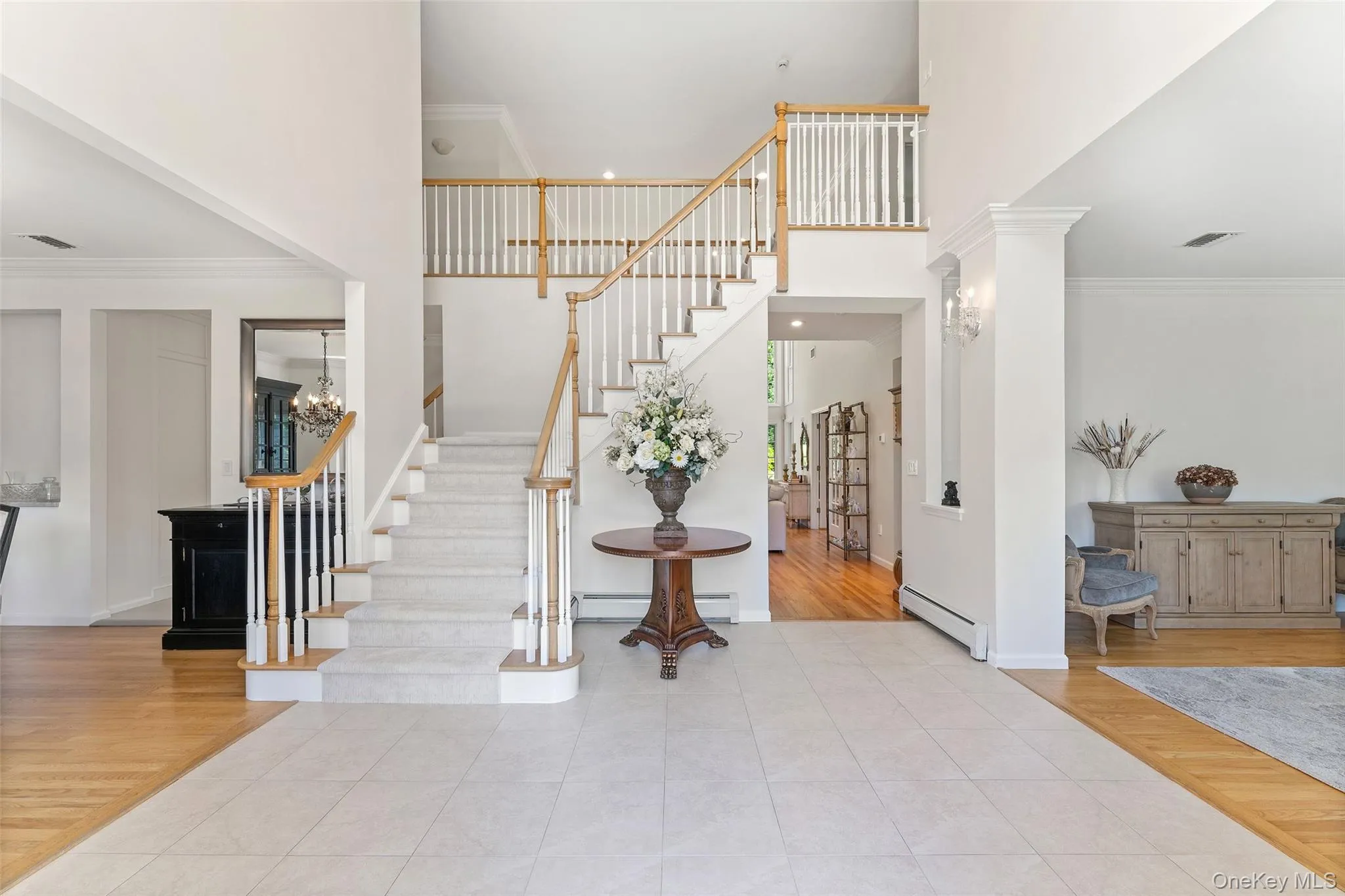 Entrance foyer featuring ornamental molding, wood finished floors, a towering ceiling, stairs, and a baseboard radiator Entrance foyer featuring ornamental molding, wood finished floors, a towering ceiling, stairs, and a baseboard radiator