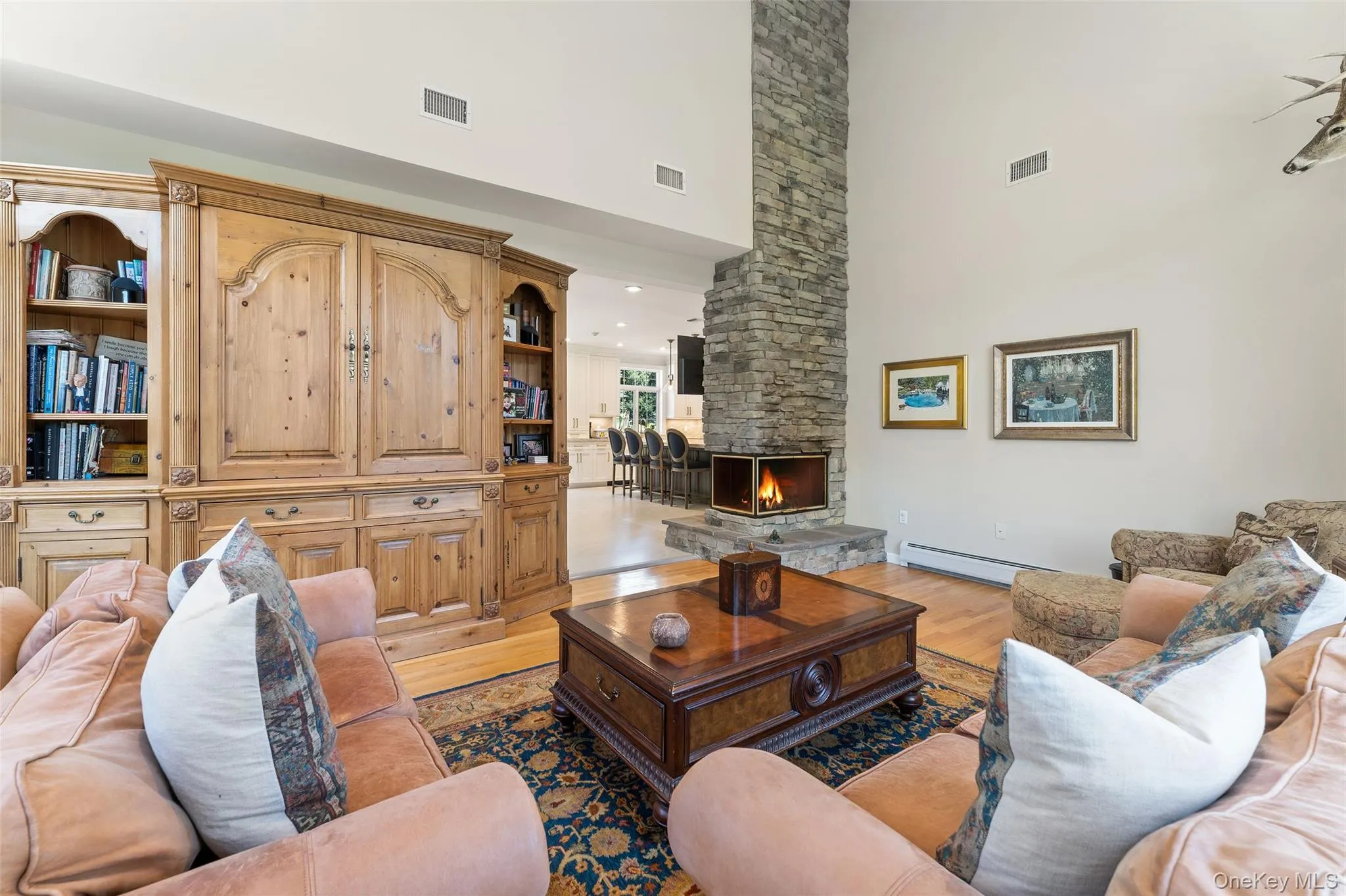 Living area featuring a high ceiling, light wood finished floors, and a stone fireplace Living area featuring a high ceiling, light wood finished floors, and a stone fireplace