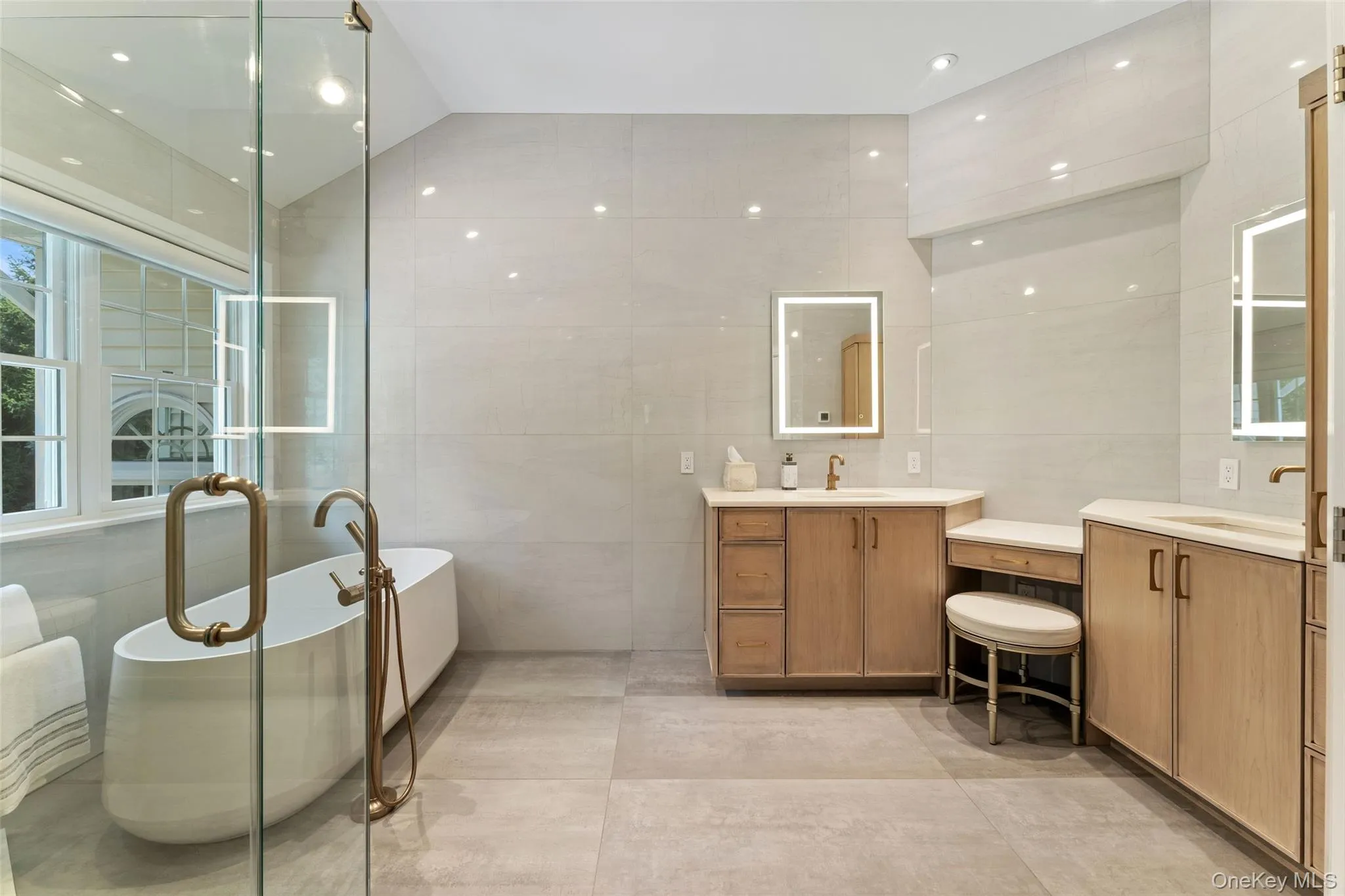 Bathroom with healthy amount of natural light, two vanities, tile walls, recessed lighting, and a freestanding tub Bathroom with healthy amount of natural light, two vanities, tile walls, recessed lighting, and a freestanding tub