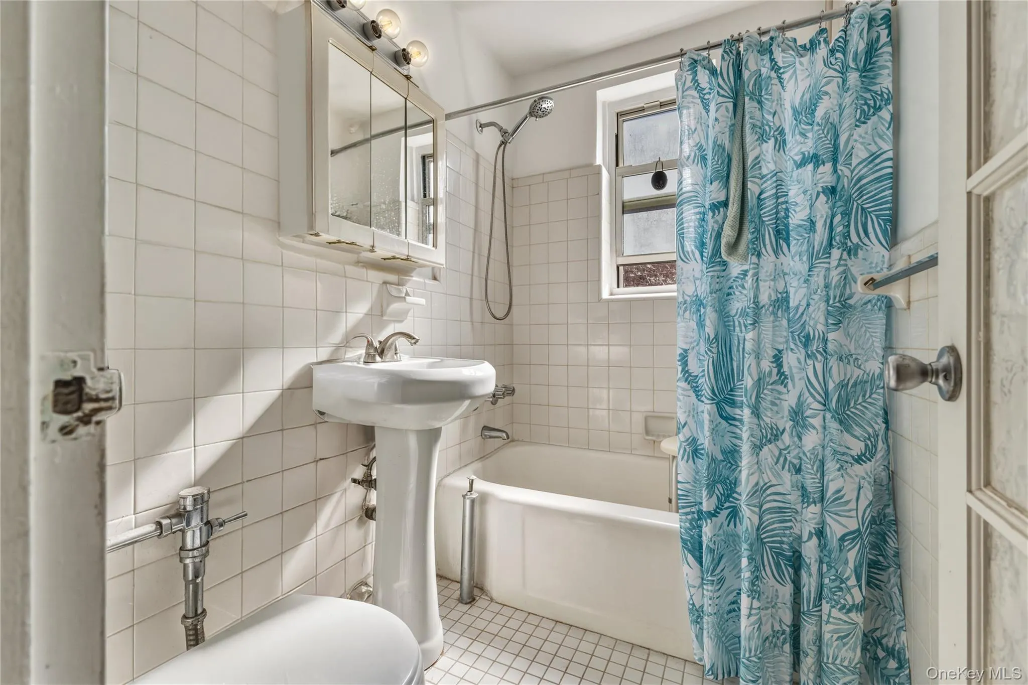 Bathroom featuring white tiled walls and a white pedestal sink Bathroom featuring white tiled walls and a white pedestal sink