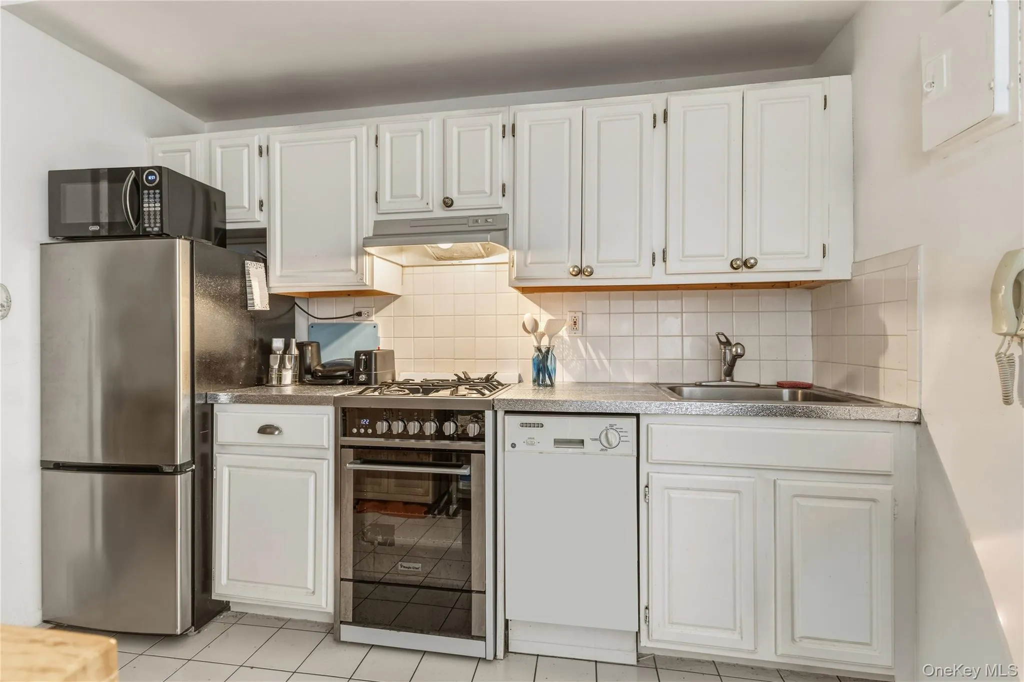 Kitchen with white shaker-style cabinetry, a stainless steel refrigerator, an integrated oven and cooktop, a built-in dishwasher, and a tile backsplash Kitchen with white shaker-style cabinetry, a stainless steel refrigerator, an integrated oven and cooktop, a built-in dishwasher, and a tile backsplash