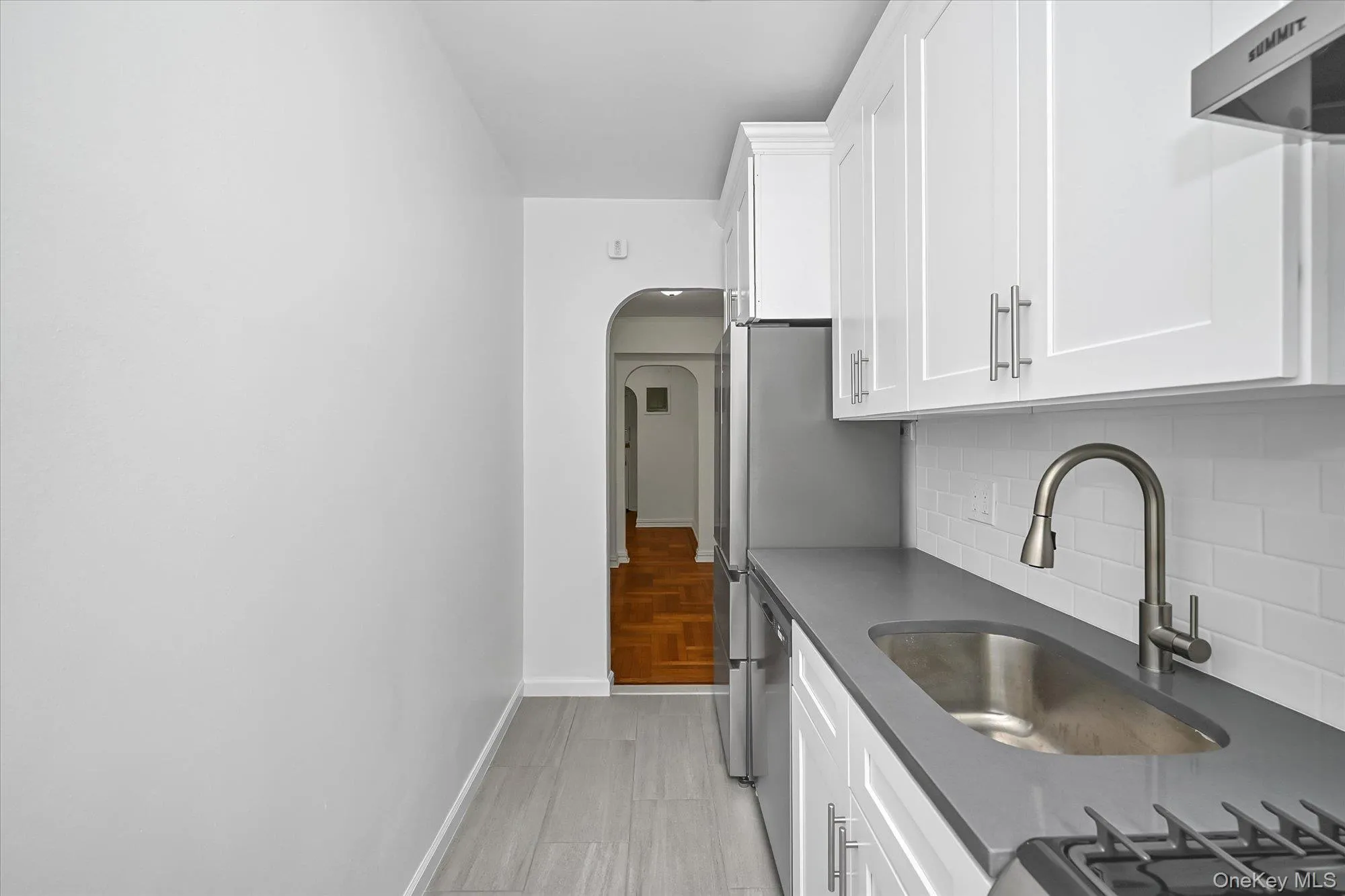 Kitchen featuring white shaker-style cabinetry, a stainless steel sink with a pull-down faucet, a white subway tile backsplash, and dark countertops. Kitchen featuring white shaker-style cabinetry, a stainless steel sink with a pull-down faucet, a white subway tile backsplash, and dark countertops.