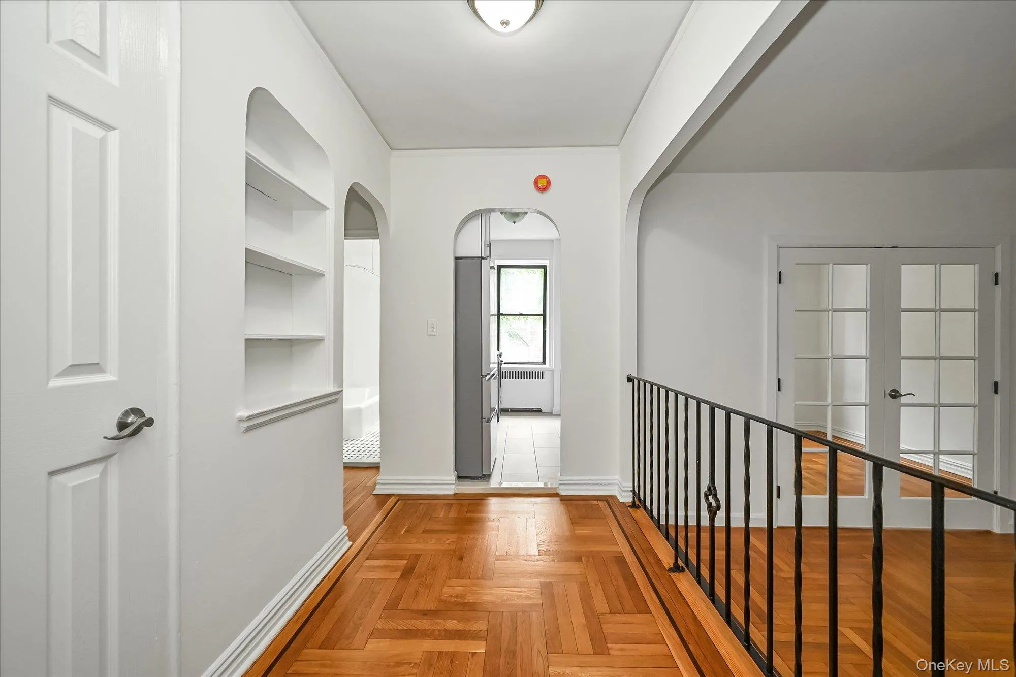 Hallway featuring herringbone wood-finish flooring, built-in shelving, archways, and a black wrought iron railing. Hallway featuring herringbone wood-finish flooring, built-in shelving, archways, and a black wrought iron railing.