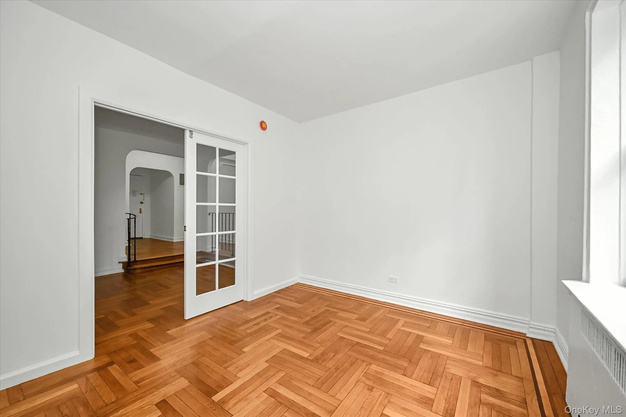 Room featuring herringbone wood-finish flooring with border detailing, white baseboards, and a glass-paneled sliding pocket door. Room featuring herringbone wood-finish flooring with border detailing, white baseboards, and a glass-paneled sliding pocket door.