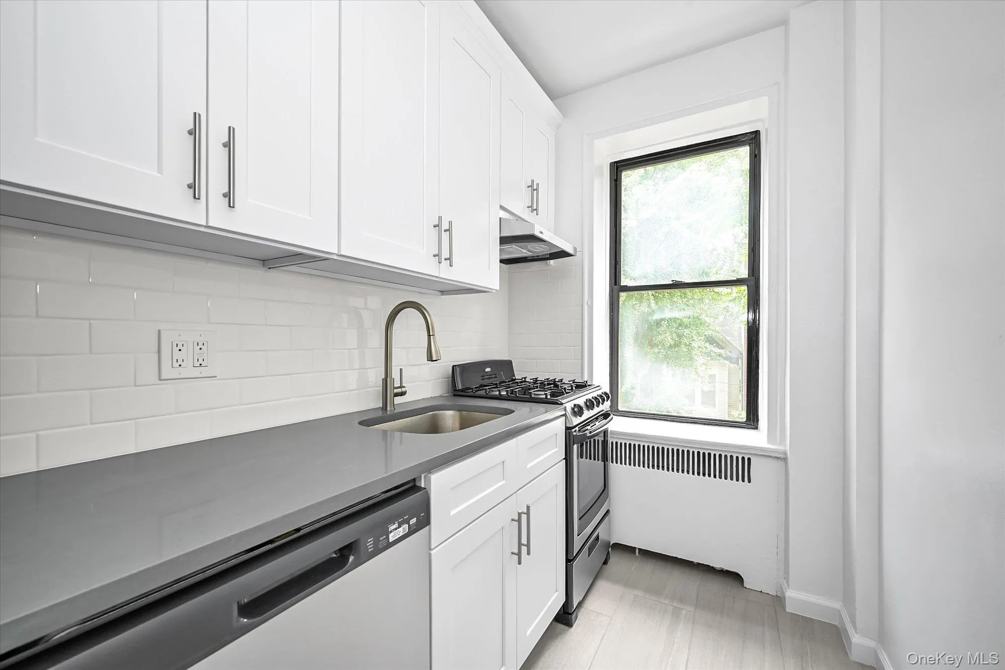 Modern kitchen featuring white shaker cabinetry, stainless steel appliances, a grey countertop, and subway tile backsplash. Modern kitchen featuring white shaker cabinetry, stainless steel appliances, a grey countertop, and subway tile backsplash.