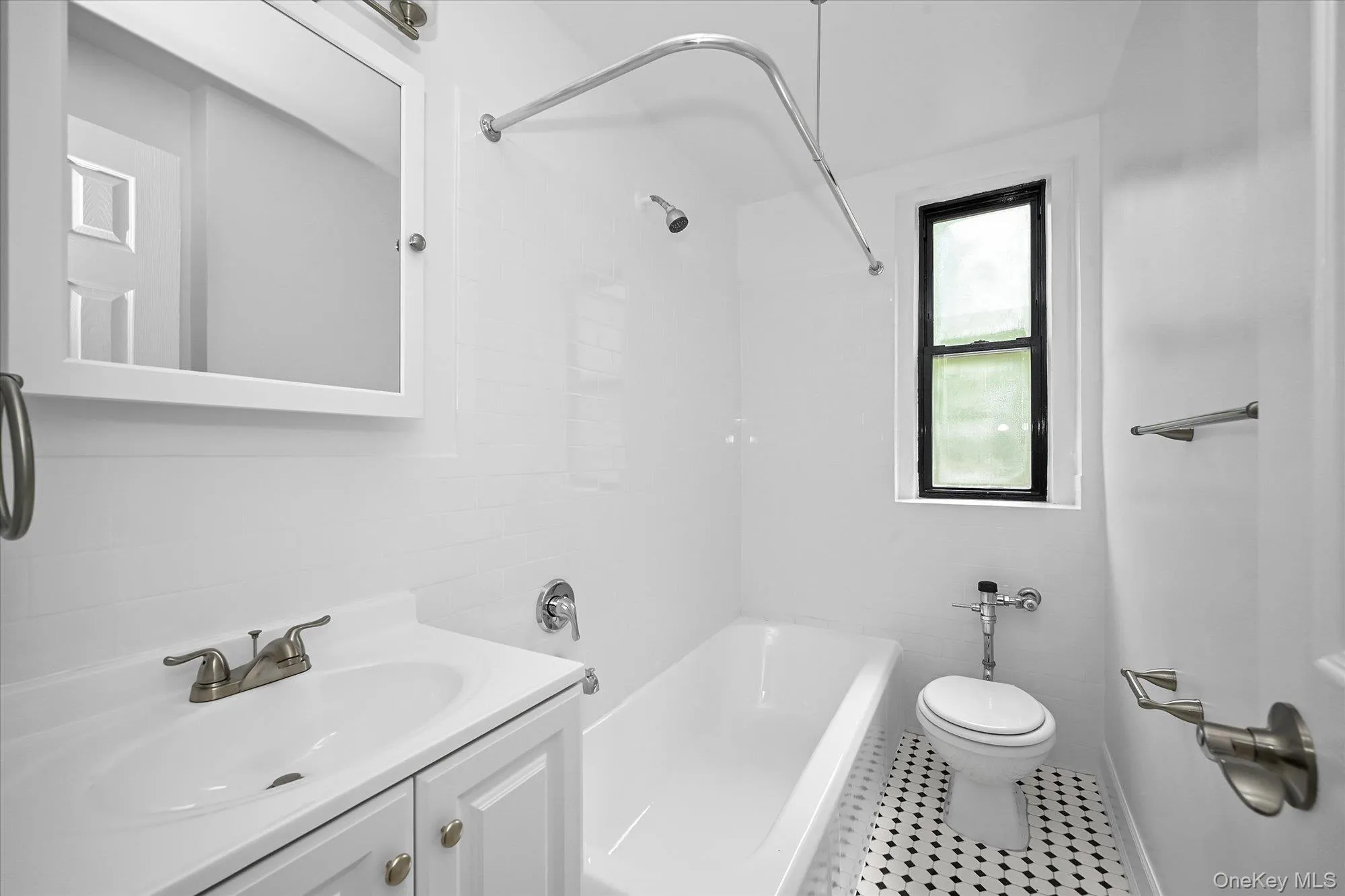 Bathroom featuring a white vanity with integrated sink, brushed nickel faucet, wall-mounted medicine cabinet with integrated lighting, white subway tile shower surround, and black and white hexagonal floor tiling. Bathroom featuring a white vanity with integrated sink, brushed nickel faucet, wall-mounted medicine cabinet with integrated lighting, white subway tile shower surround, and black and white hexagonal floor tiling.