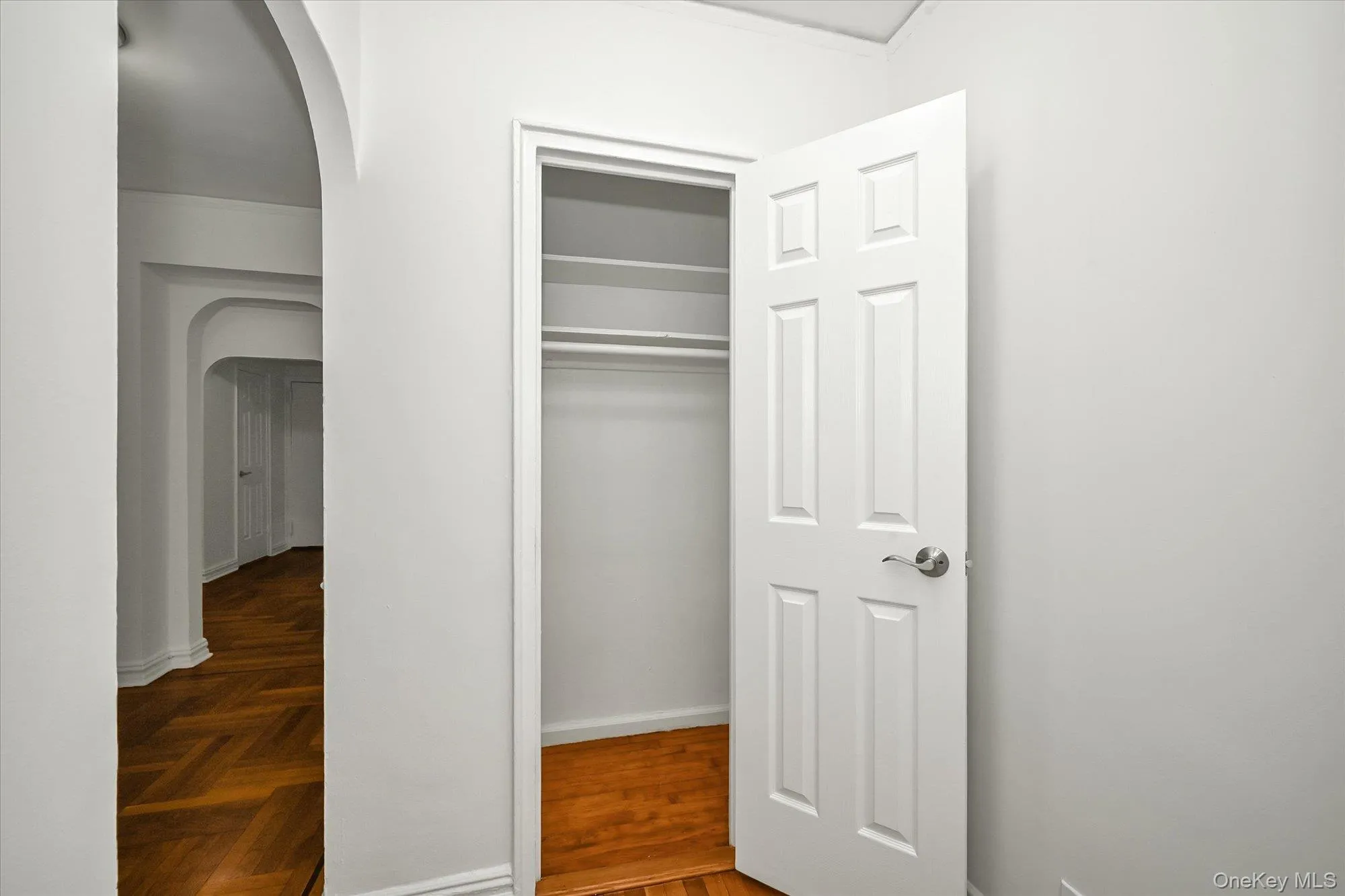 Closet with shelving and hanging rod, wood-finish flooring, and arched entryway. Closet with shelving and hanging rod, wood-finish flooring, and arched entryway.
