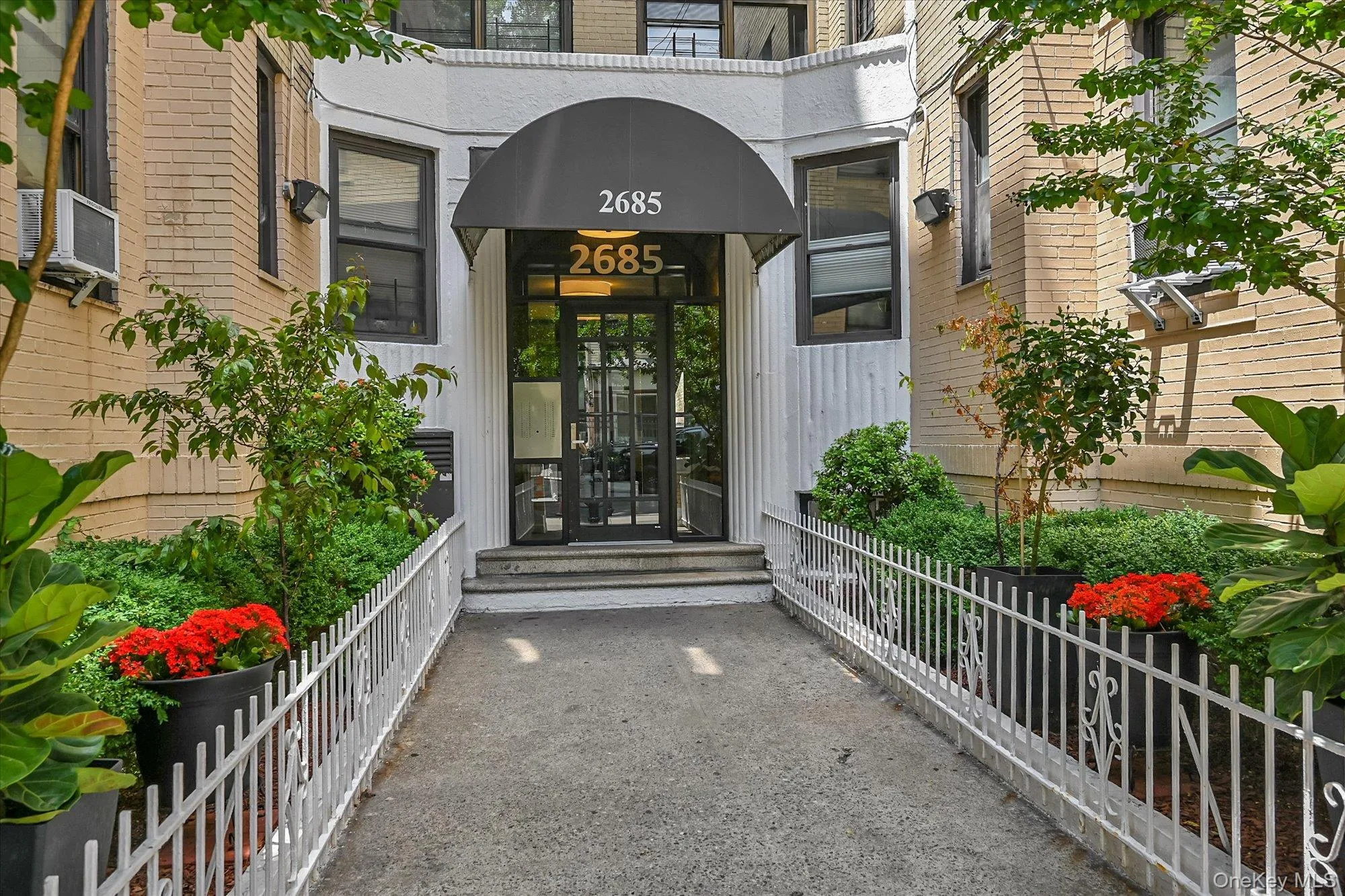 Building entrance featuring a dark awning, glass doors with dark framing, and a concrete pathway Building entrance featuring a dark awning, glass doors with dark framing, and a concrete pathway