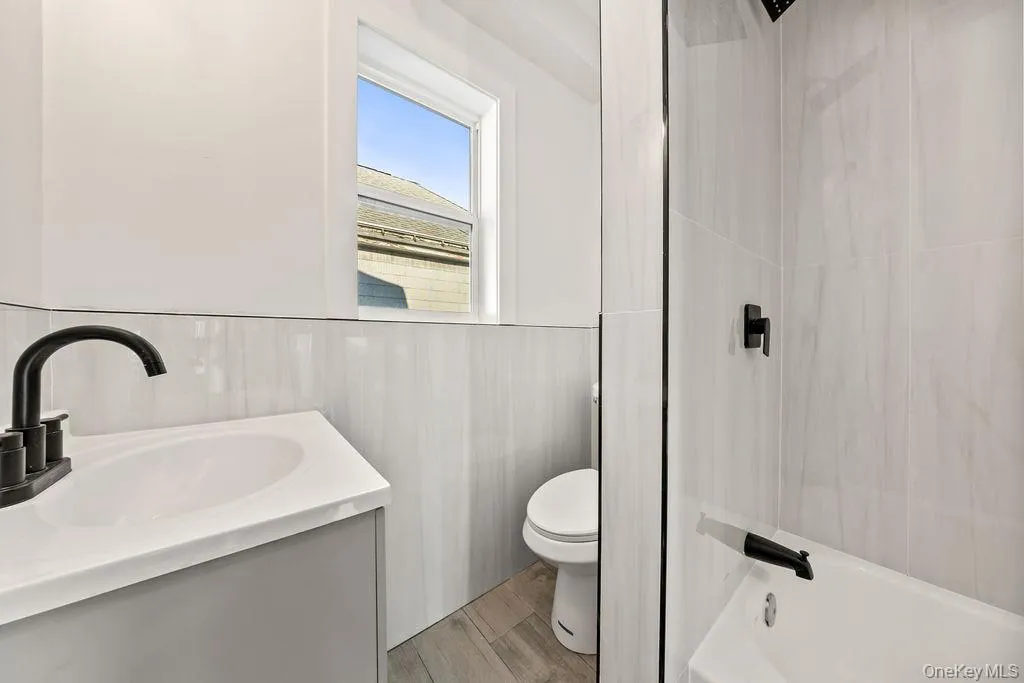 Bathroom featuring vanity, a wainscoted wall, bathing tub / shower combination, and wood finish floors Bathroom featuring vanity, a wainscoted wall, bathing tub / shower combination, and wood finish floors