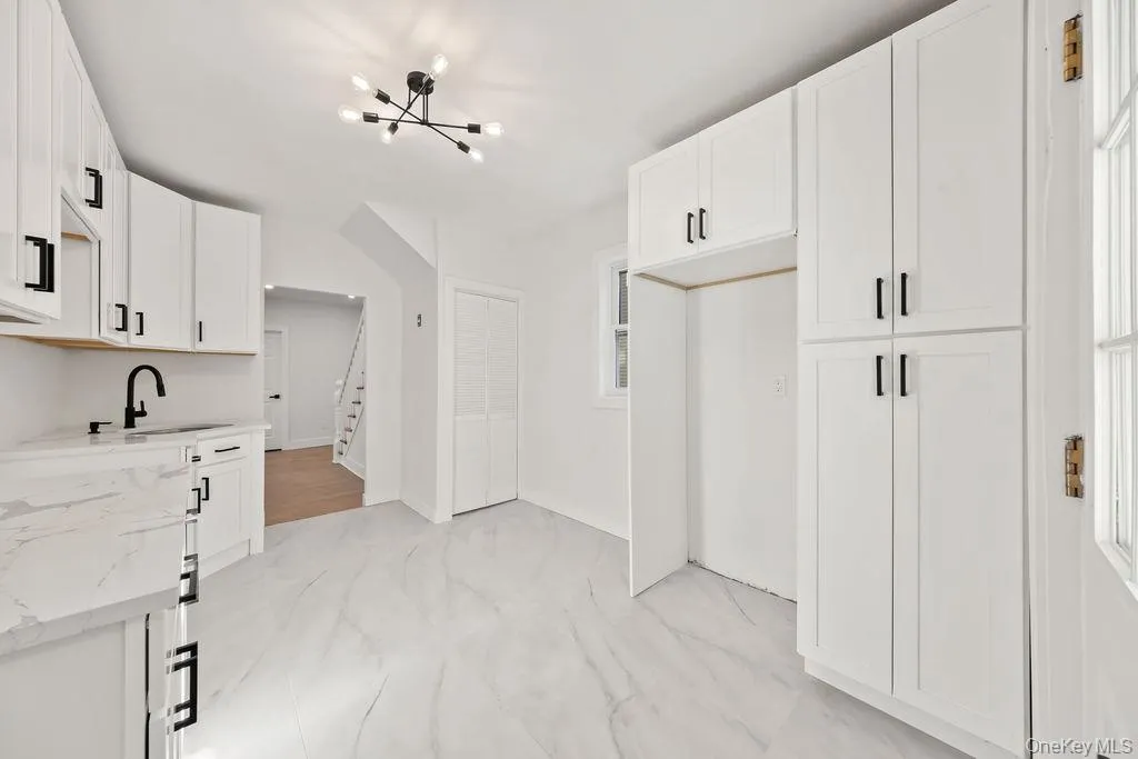 Kitchen with a chandelier, light marble finish floors, white cabinetry, and light stone countertops Kitchen with a chandelier, light marble finish floors, white cabinetry, and light stone countertops