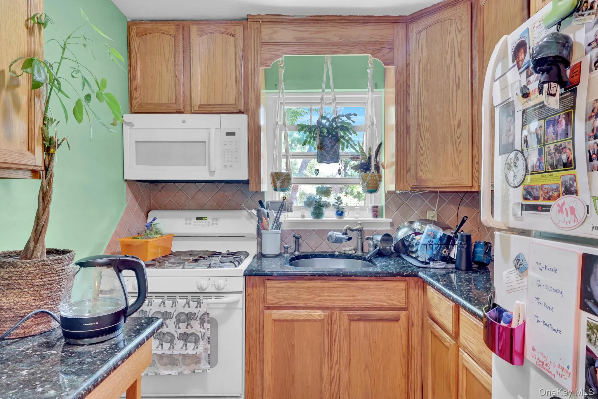 Kitchen featuring light wood cabinetry, dark speckled countertops, white appliances, and a tiled backsplash Kitchen featuring light wood cabinetry, dark speckled countertops, white appliances, and a tiled backsplash