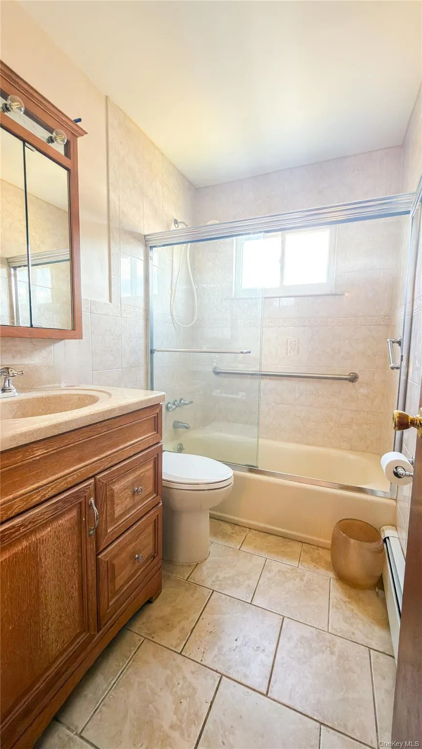 Full bathroom with tub / shower combo and glass doors, vanity with wood cabinets and tile floors Full bathroom with tub / shower combo and glass doors, vanity with wood cabinets and tile floors